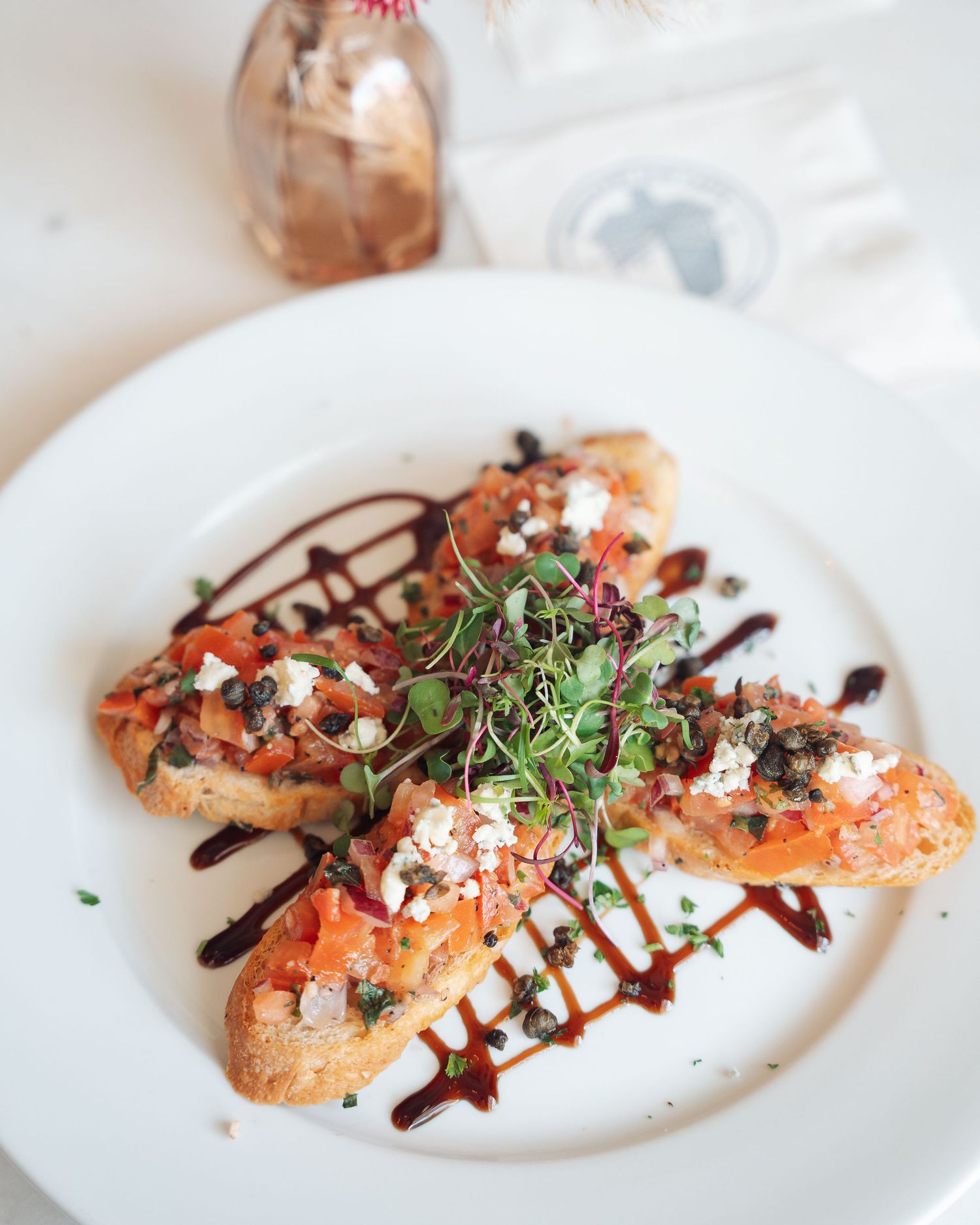 Toasted bruschetta topped with tomatoes, capers, feta cheese, microgreens, and balsamic glaze.