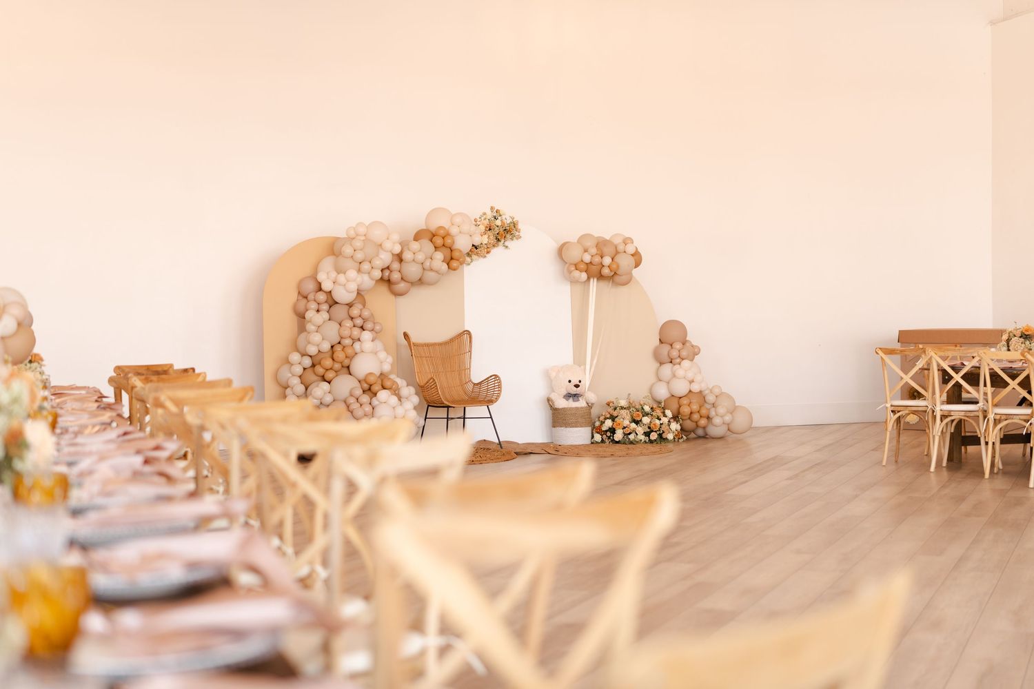 Boho-style event venue with long decorated tables, balloon arch, and neutral color palette decor.