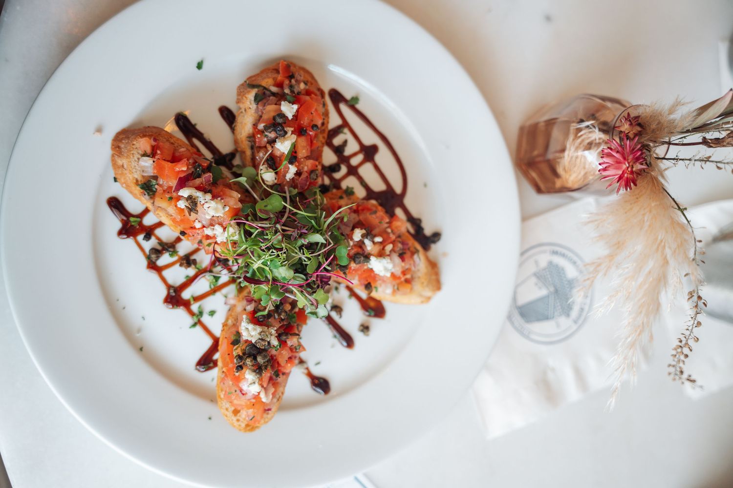 Bruschetta with tomatoes, feta, microgreens, and balsamic drizzle on a white plate.