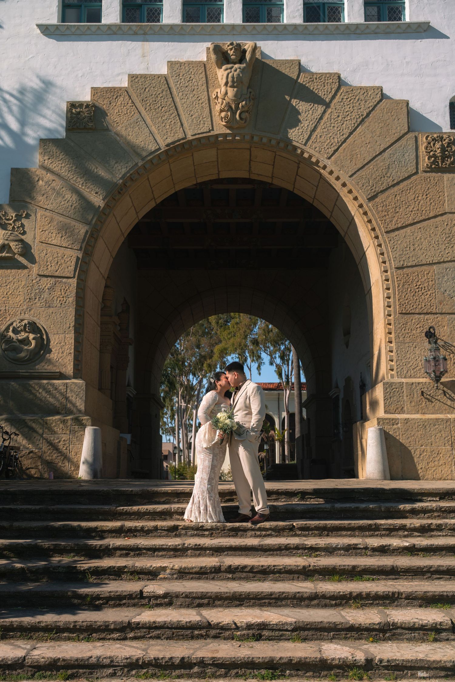 Bride and groom kissing under ornate stone arch on steps at Santa Barbara Courthouse wedding.