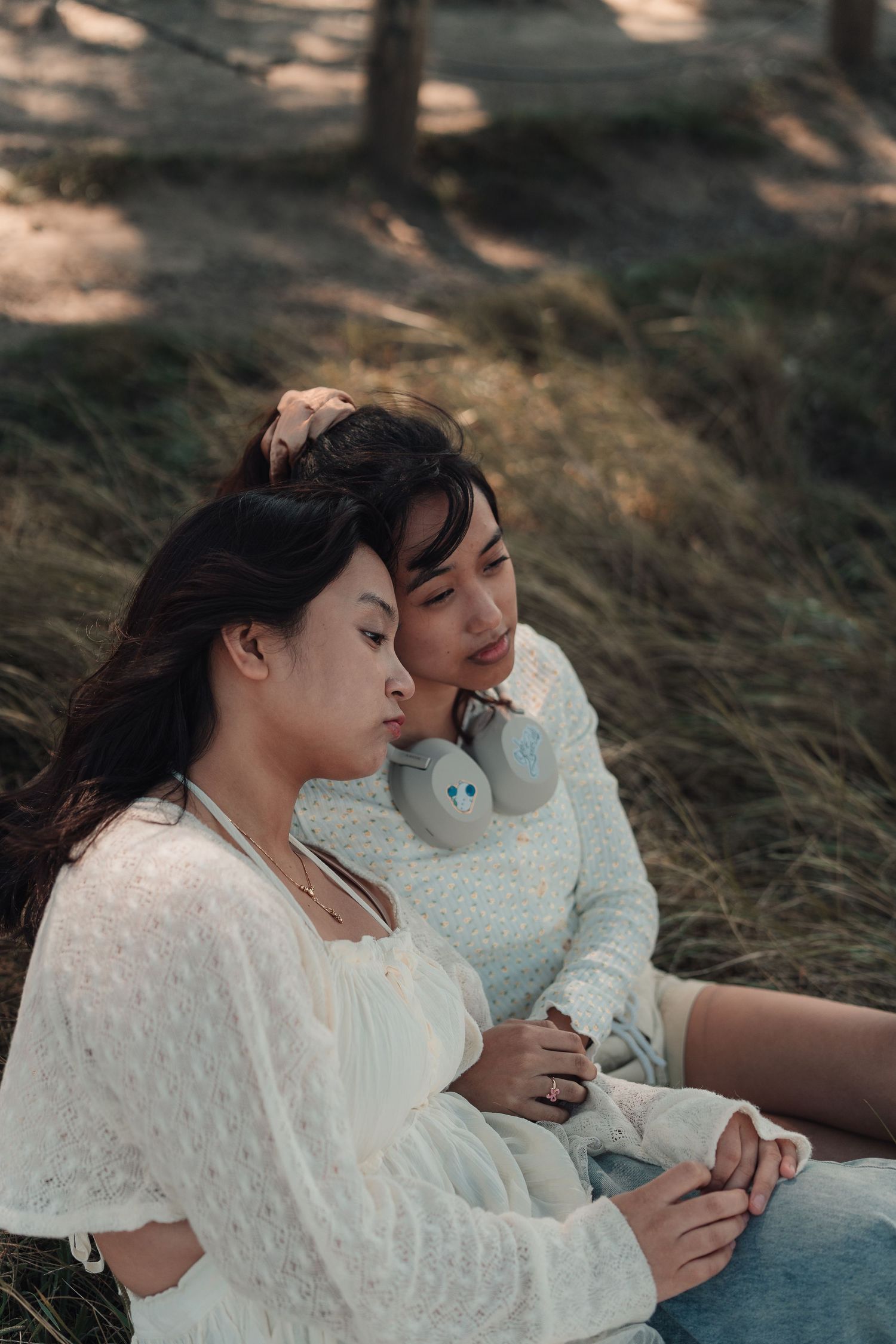 Two young women sitting together in a peaceful outdoor setting, eyes closed, leaning on each other.