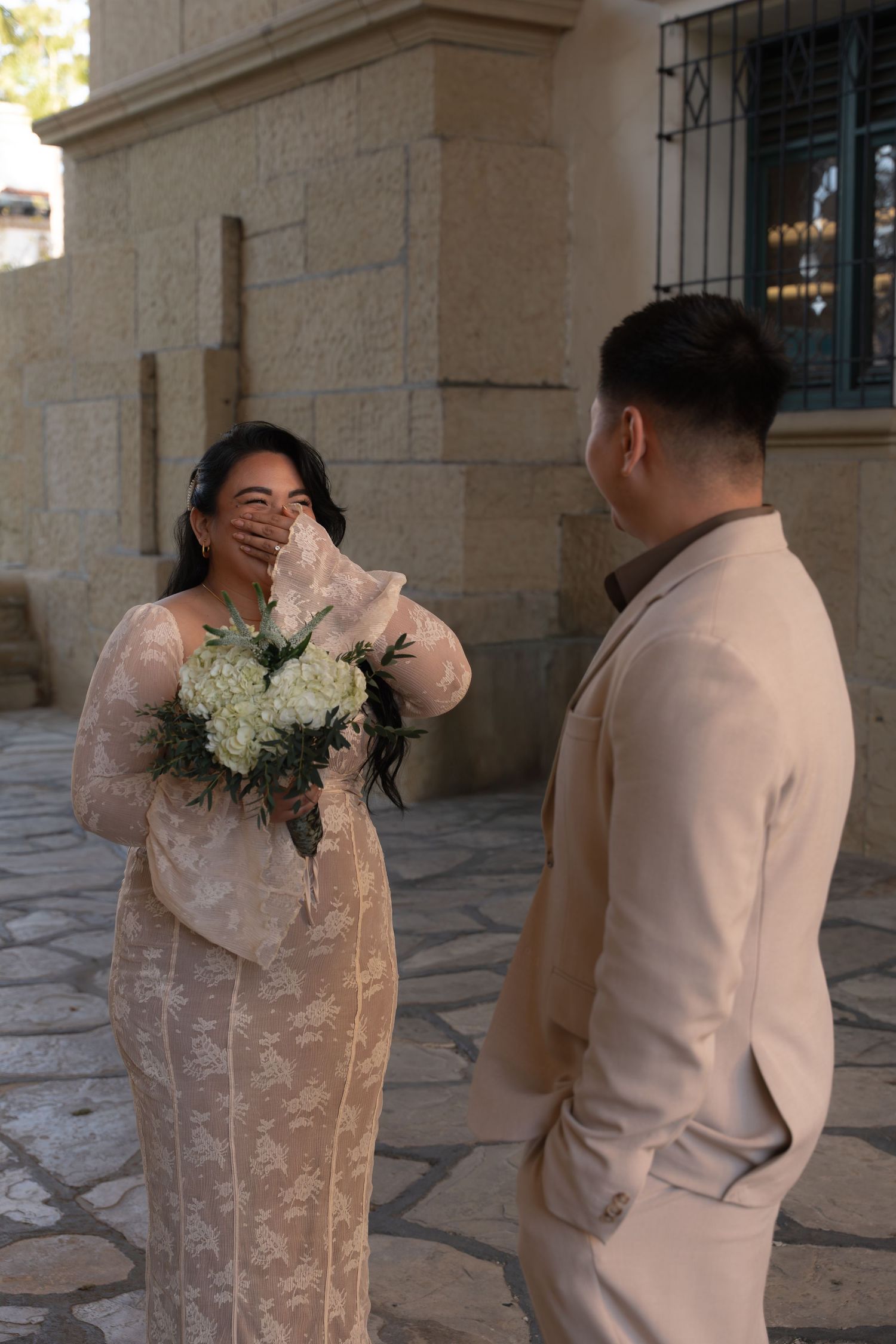 Emotional bride covers her mouth while groom looks on during outdoor first look moment.