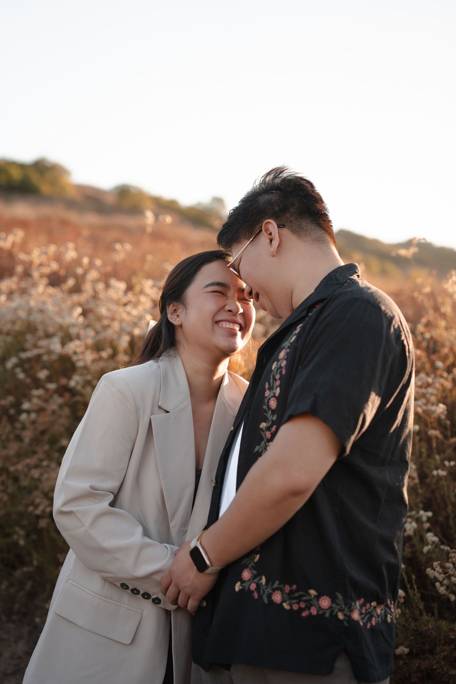 Happy Asian couple holding hands and smiling at each other in golden sunset field.
