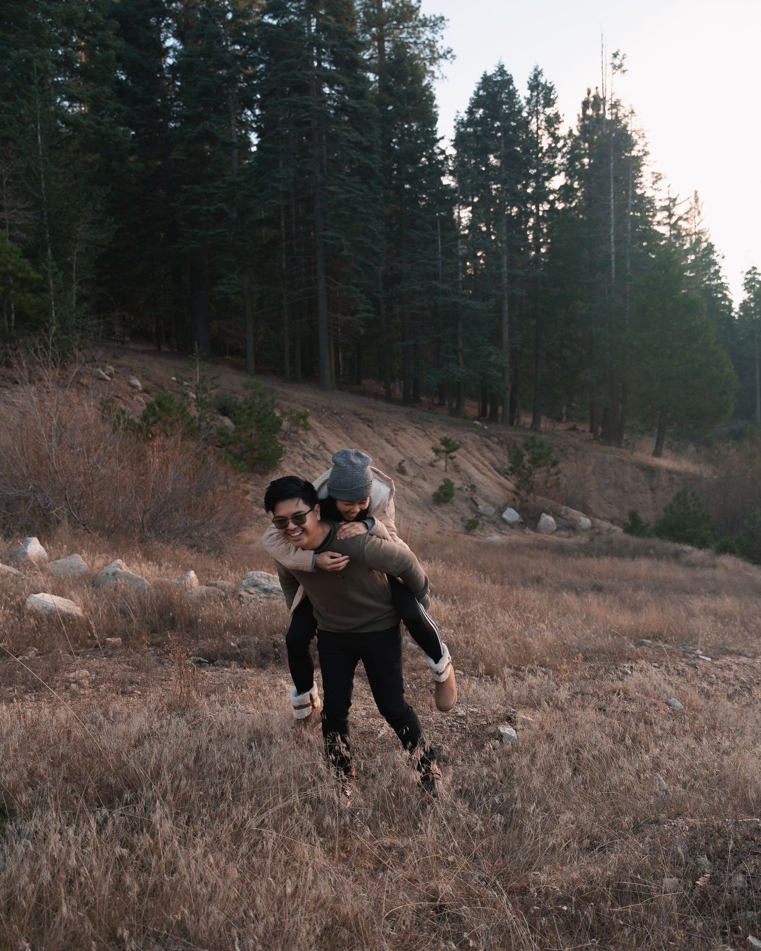 Couple enjoying piggyback ride in forest meadow at golden hour.