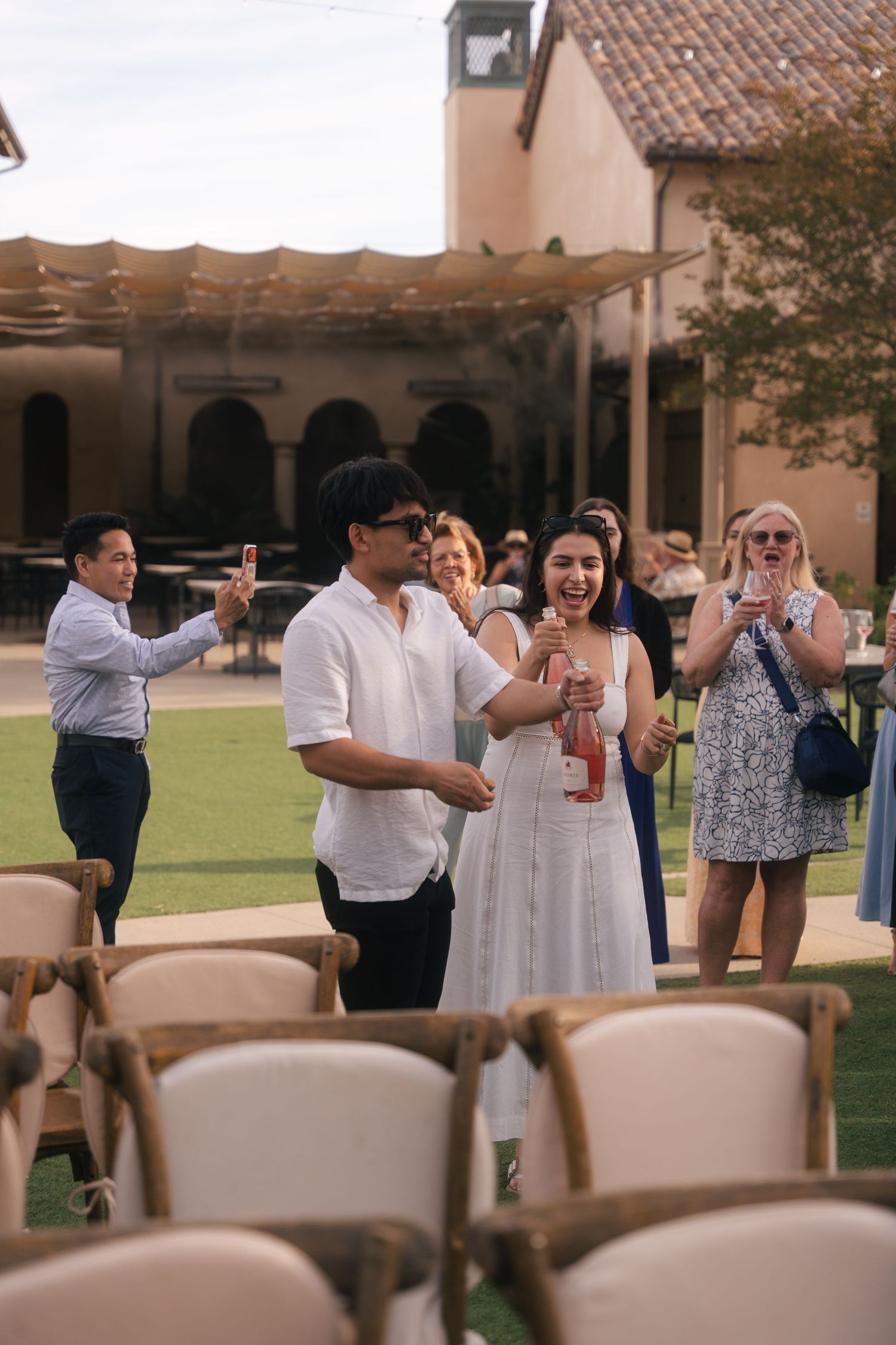 Wedding guests celebrating outdoors at a Spanish-style venue holding drinks and petals.