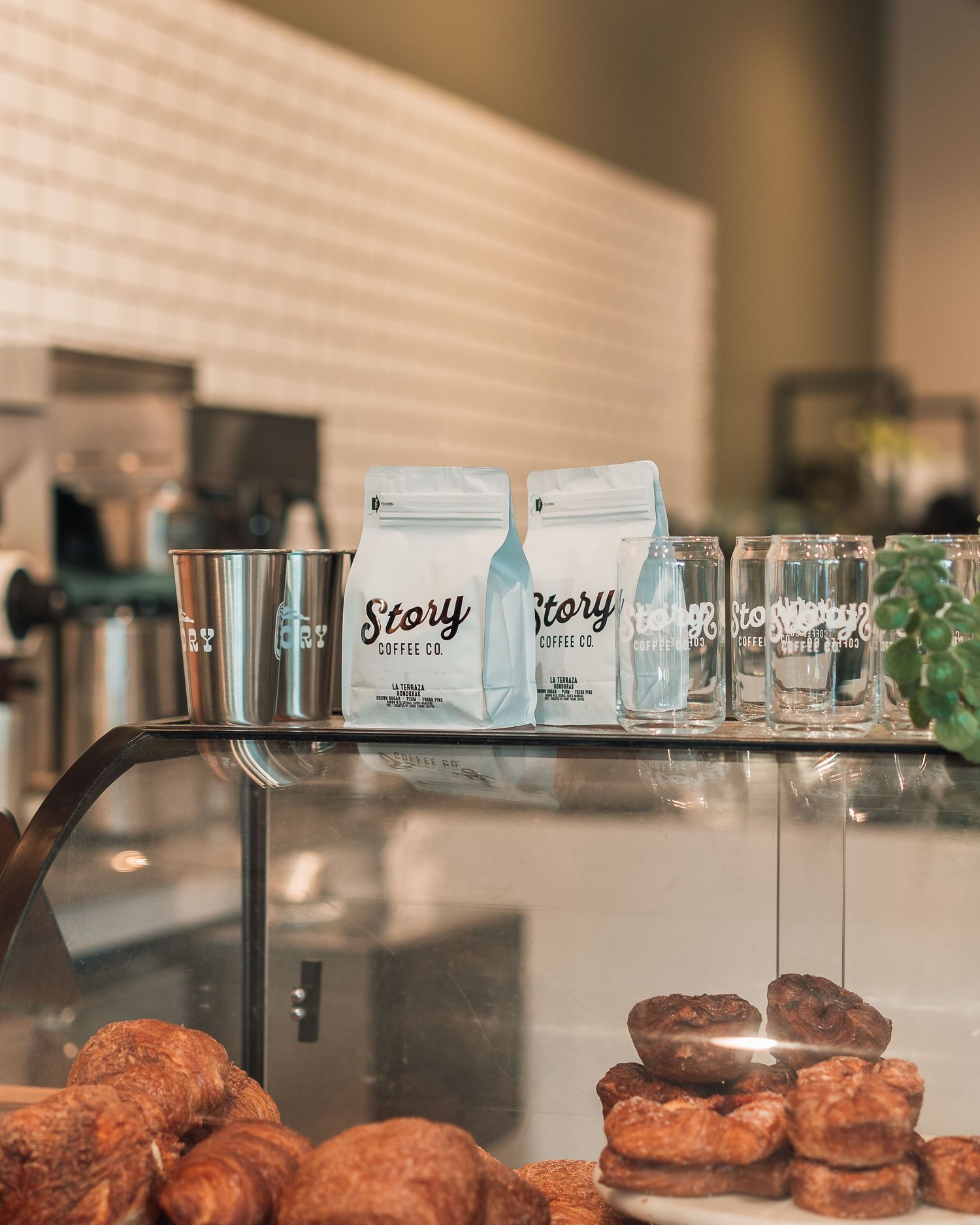 Story Coffee Co branded bags and glasses displayed above fresh pastries on a cafe counter.