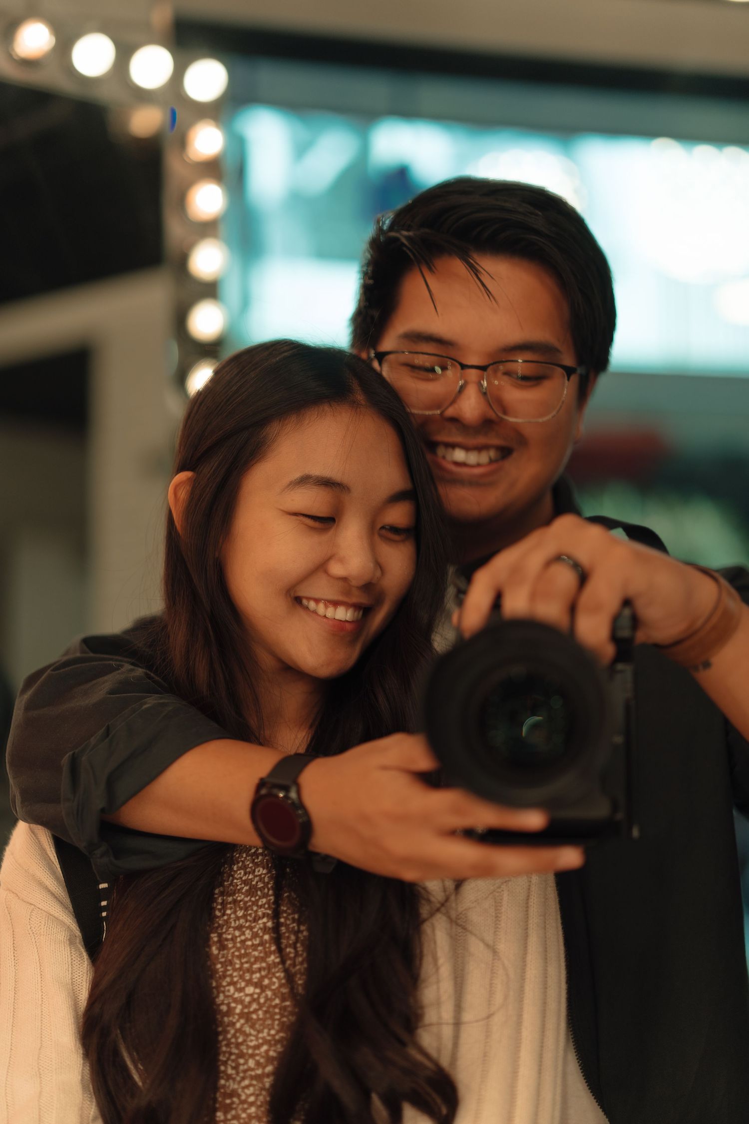 Happy Asian couple smiling while reviewing photos on camera indoors.