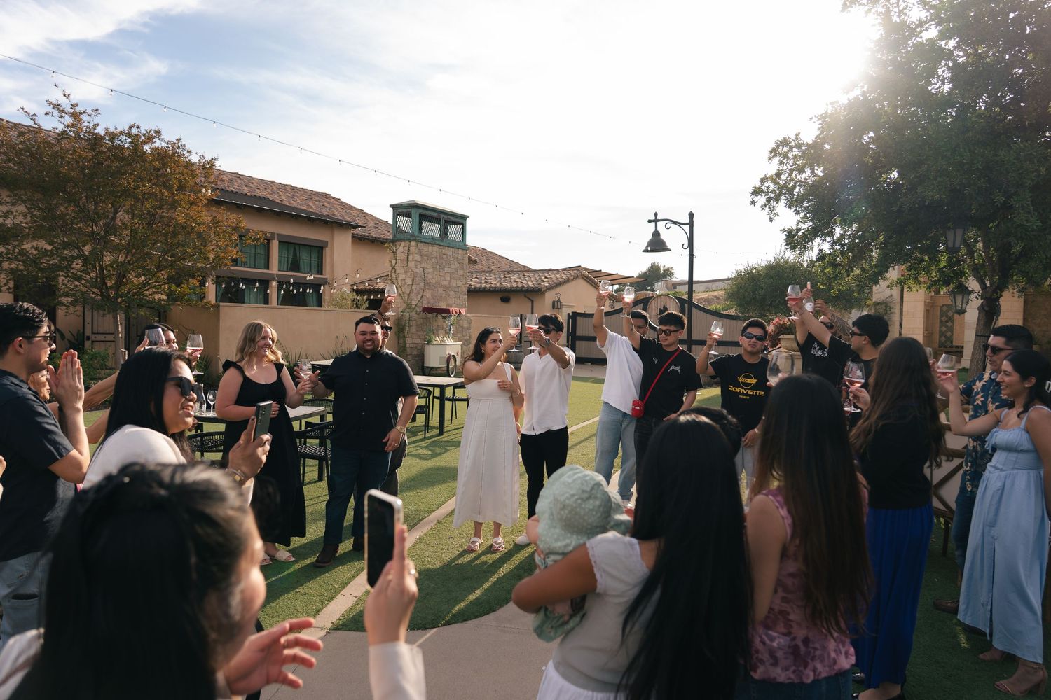 Wedding guests gathering outdoors in courtyard celebrating newlyweds in warm golden sunlight.