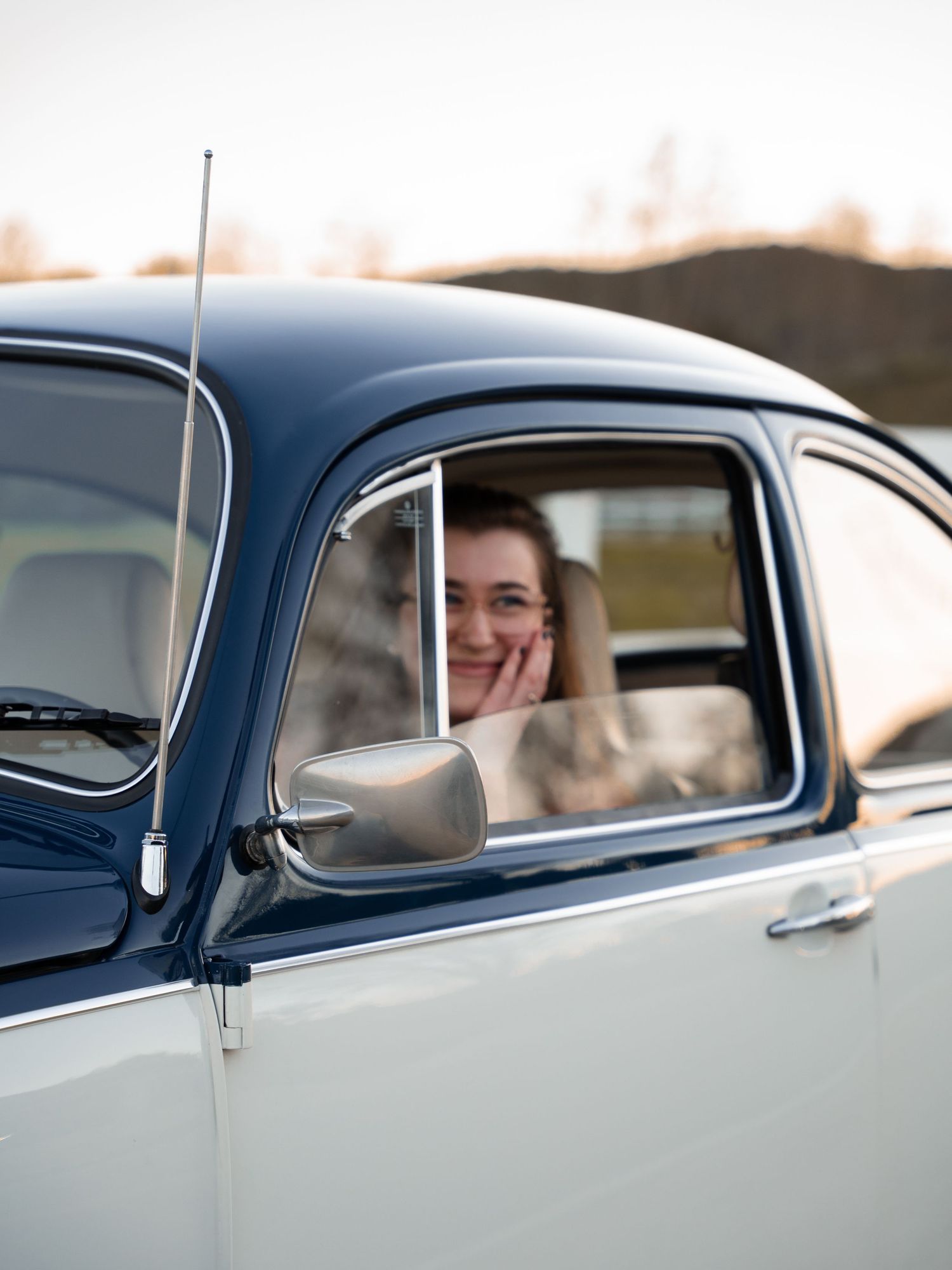 Young woman smiling inside a classic vintage blue and white car, resting her chin on her hand.