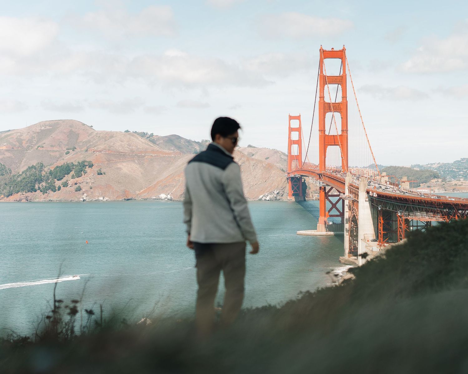 Man in gray jacket gazing at Golden Gate Bridge from scenic overlook.