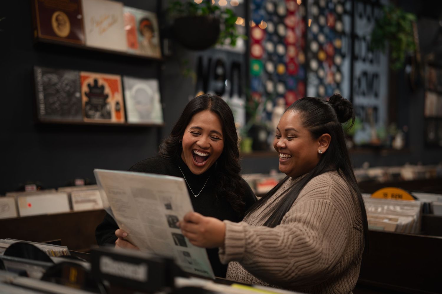 Two women laughing together while looking at a vinyl record in a record store.