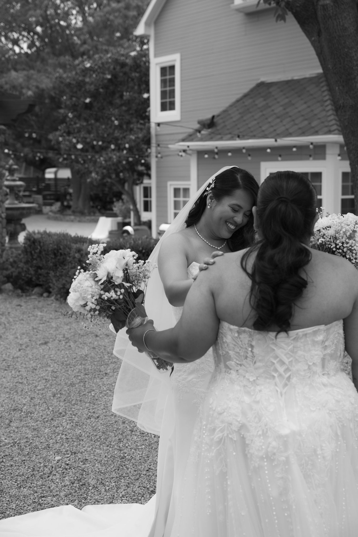 Two brides in white wedding gowns sharing an emotional first look moment in black and white photo.