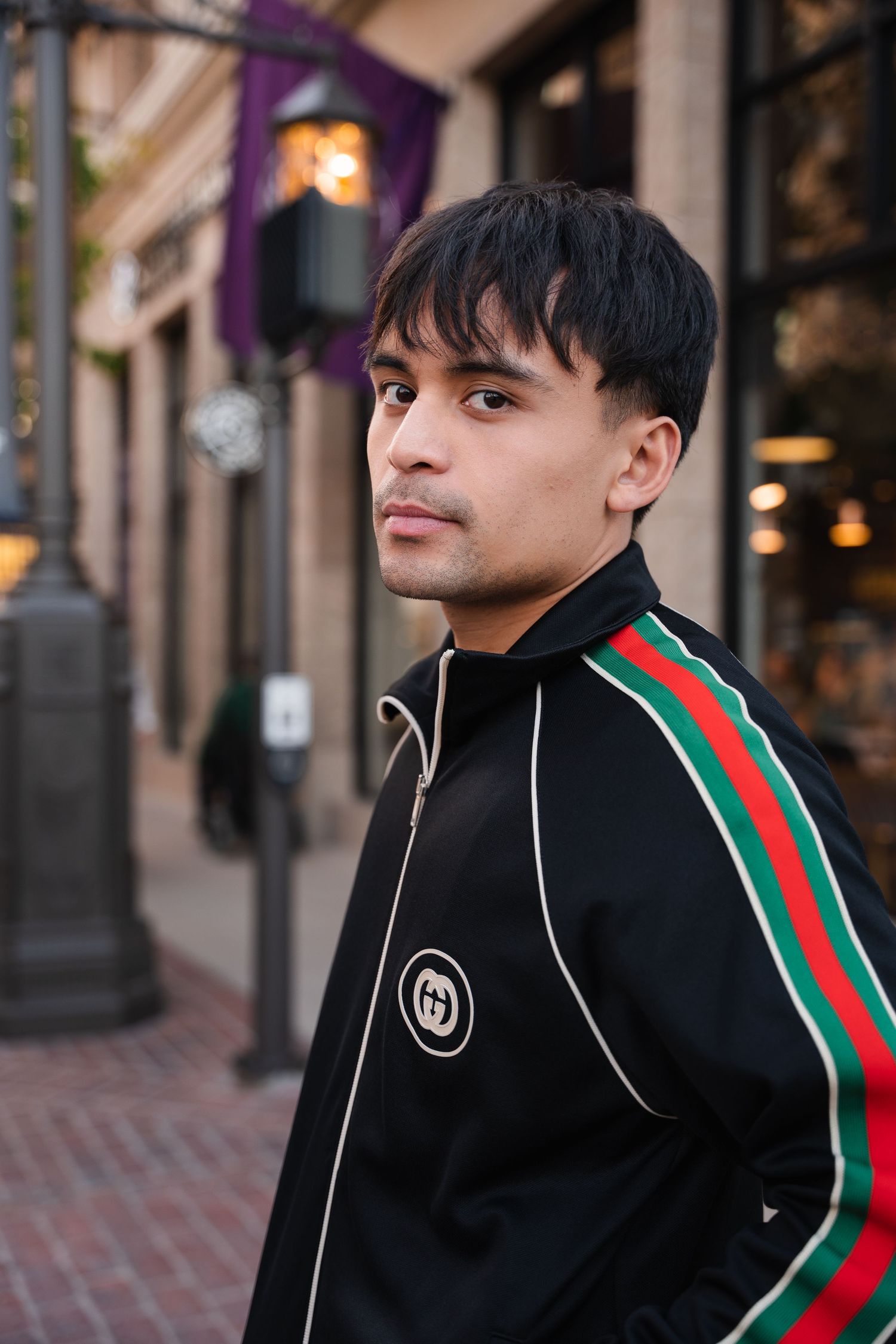 Young man in black Gucci tracksuit posing confidently on a city street at dusk.