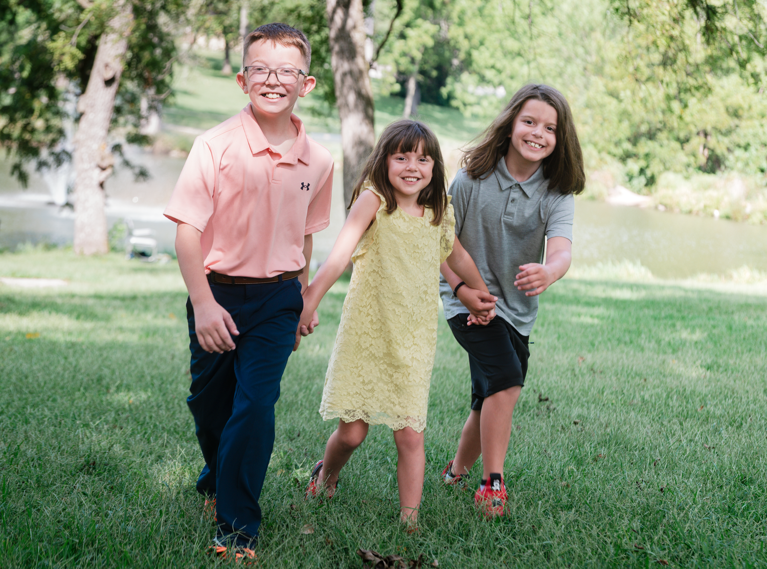 Three siblings laughing and running during a family photo session at Walnut Grove Park in Omaha