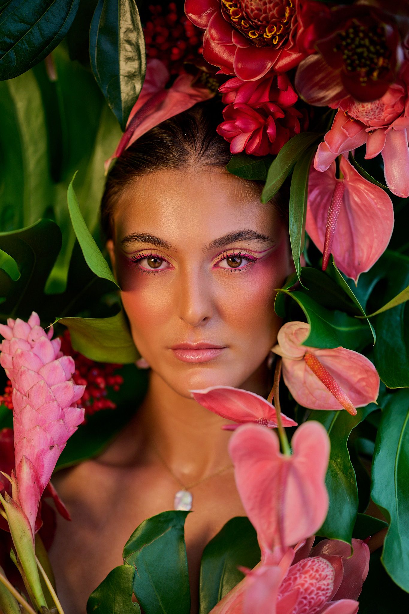 A stunning beauty portrait surrounded by vibrant pink anthurium flowers and tropical green leaves in a lush setting.