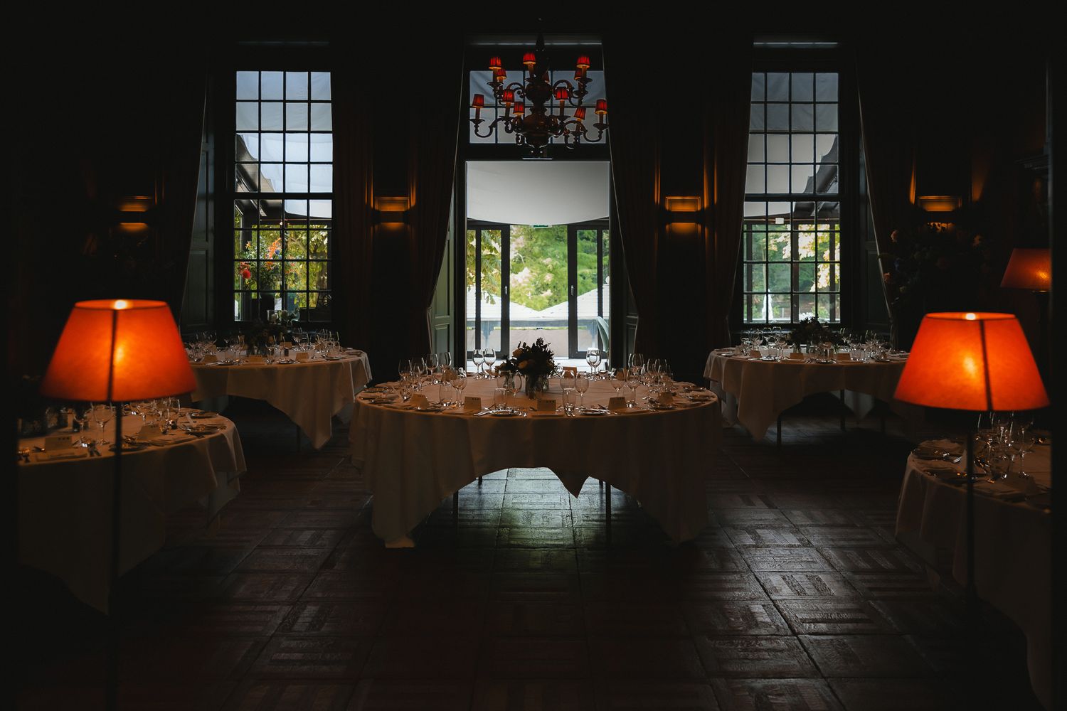 Elegant dining room setup with glowing orange table lamps and tall windows in a dimly lit restaurant interior.