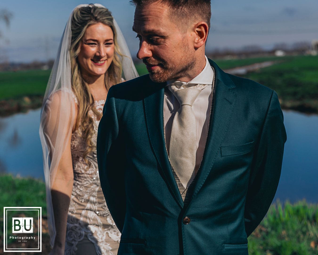 A couple shares a moment together outdoors at their wedding, with a lake in the background.