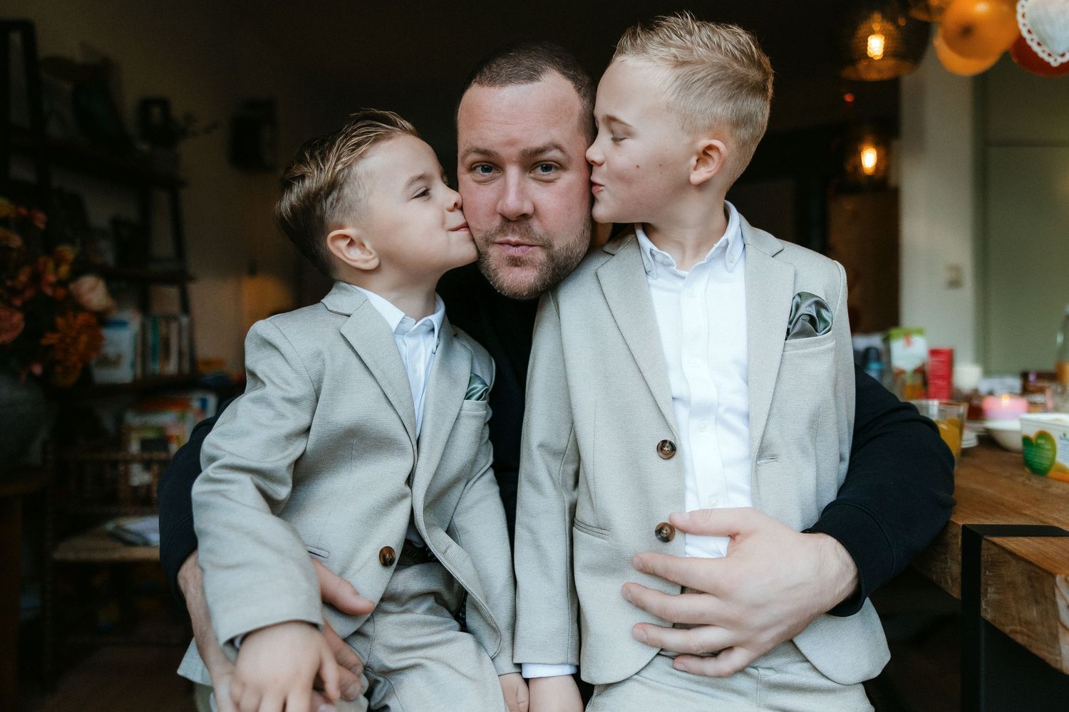 A heartwarming moment shows a parent in black receiving loving kisses from two children in matching light gray suits.