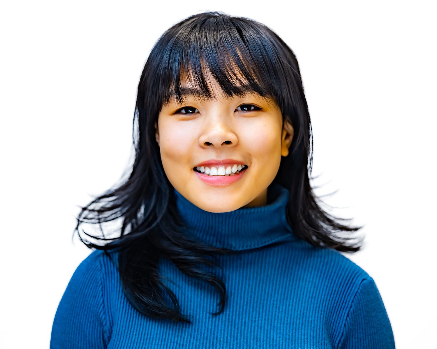 Person in blue turtleneck sweater smiling at camera against white background with black hair.