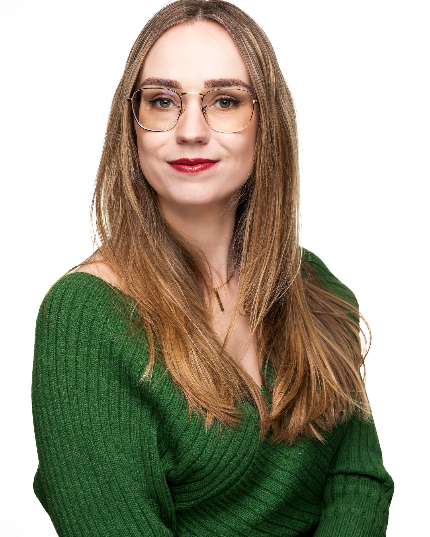 Professional portrait of a person with long blonde hair wearing glasses, red lipstick, and a green ribbed sweater.