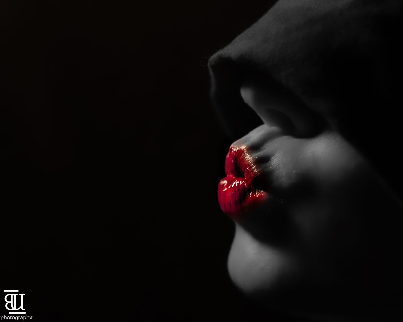 Dramatic black and white close-up photo featuring bright red lipstick on lips against dark background.