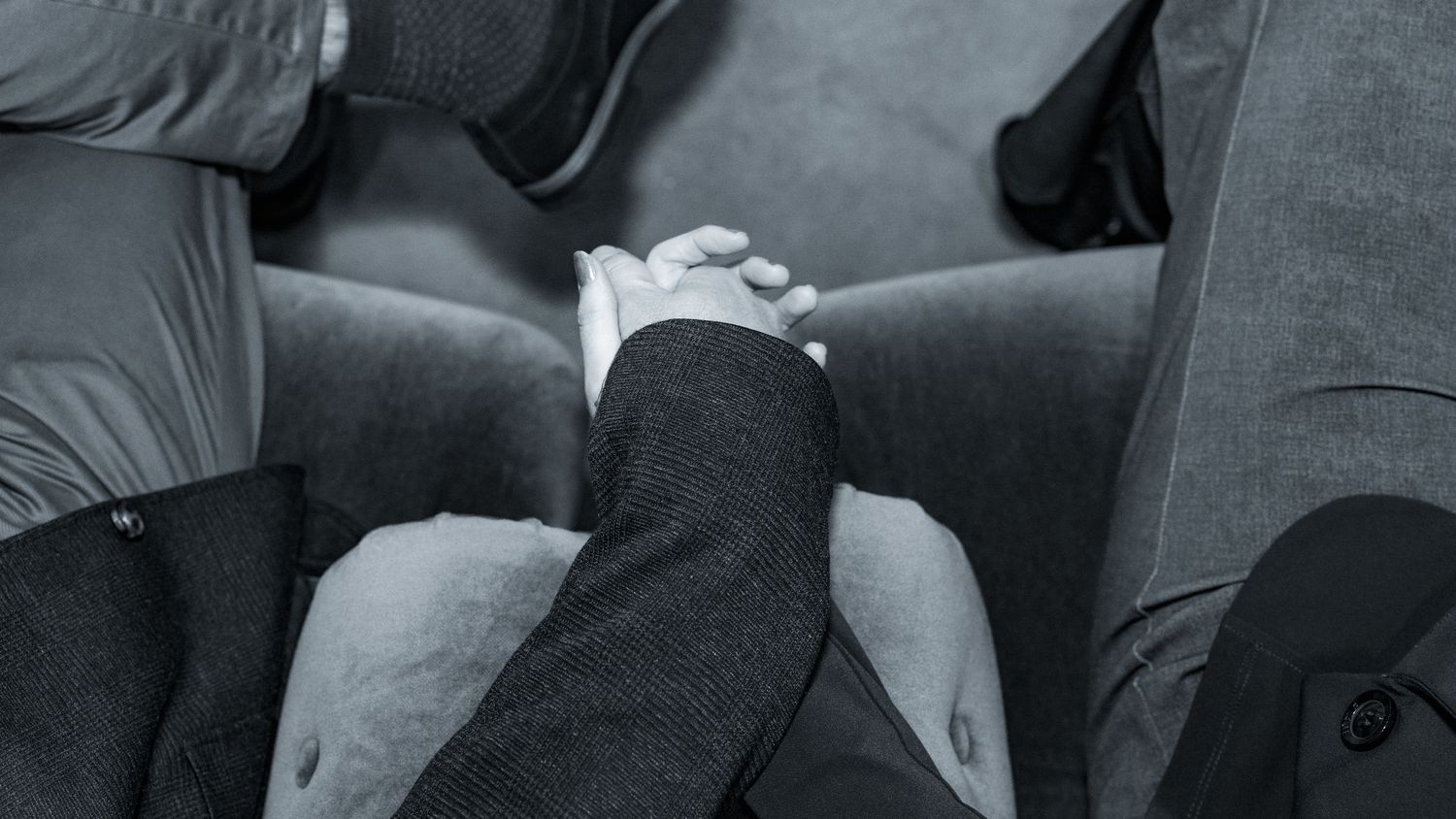A close up black and white shot of two people holding hands while sitting on a couch.