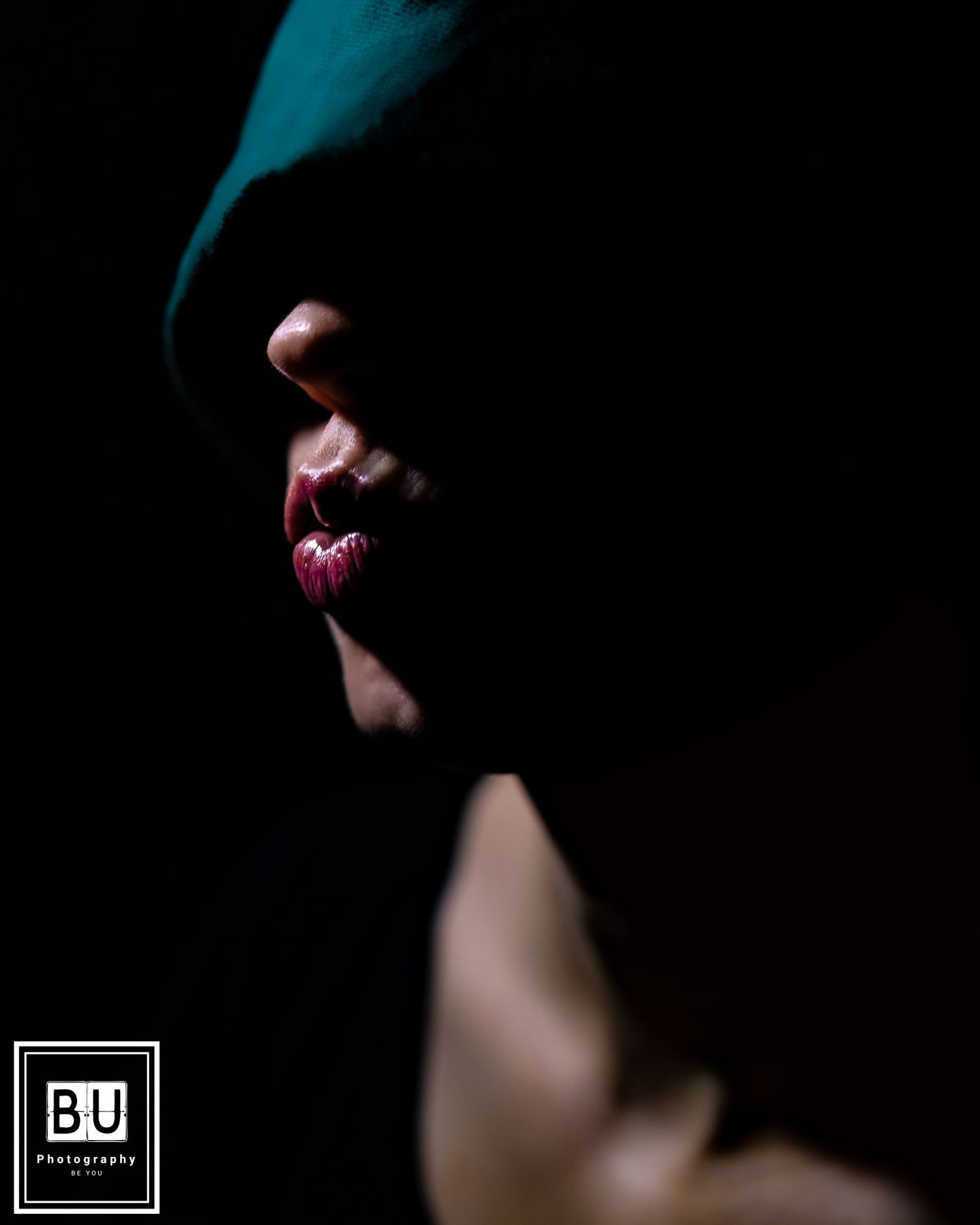 Dramatic side profile silhouette in dark lighting shows glossy pink lips against black background.