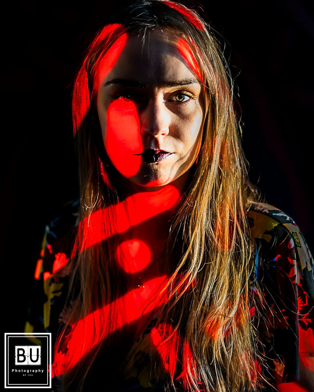 Creative portrait with striking red light patterns casting dramatic shadows across the subject.

- BU Photography -