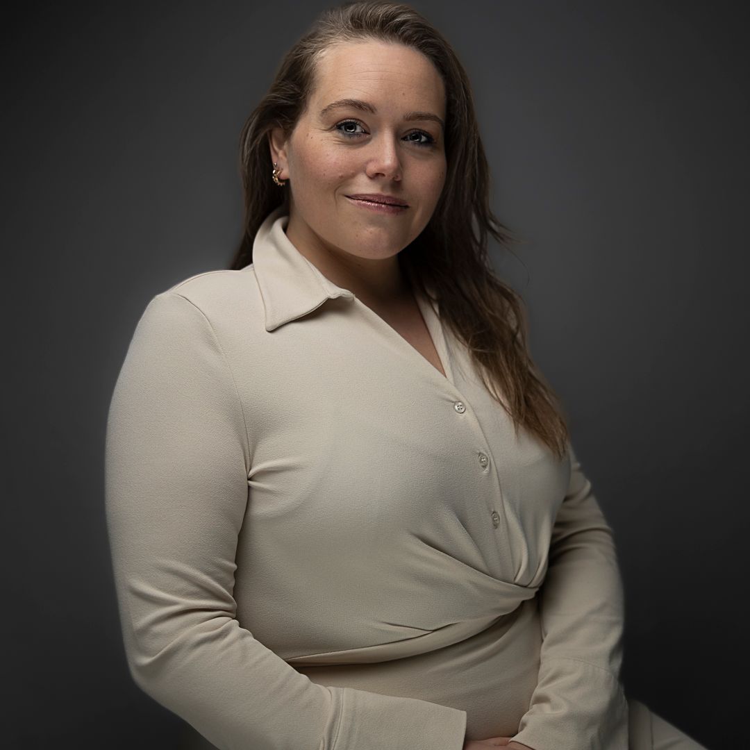 Professional studio portrait against dark background showing subject in beige button-up top with dramatic lighting.