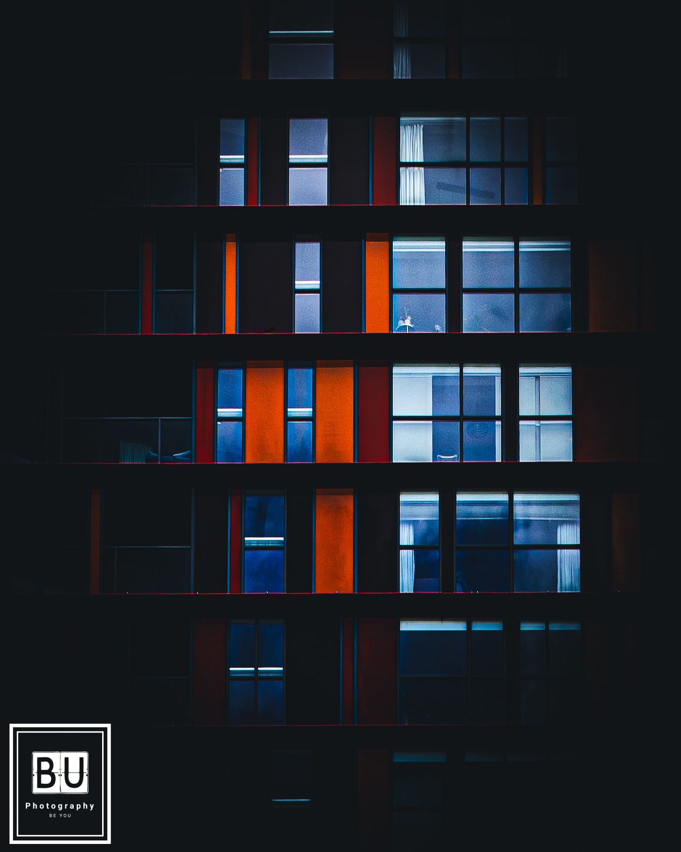 Modern apartment building facade at night with illuminated orange panels and blue-lit windows creating geometric patterns.