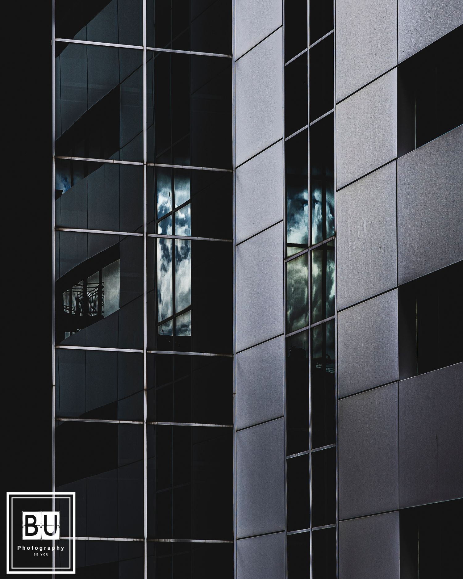 Modern office building exterior with reflective glass windows and dark geometric panels creating an abstract architectural pattern.