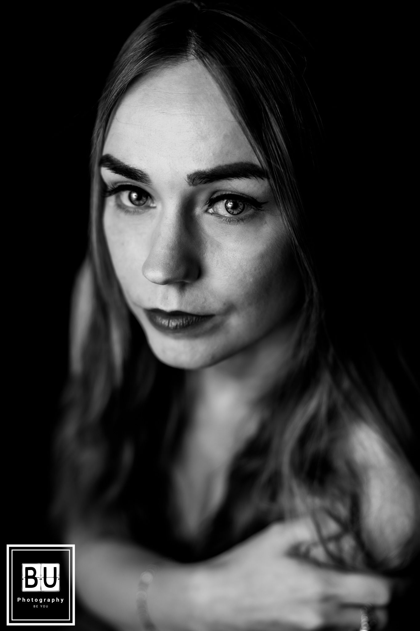 A dramatic black and white portrait showing striking eye makeup and dark lipstick in moody lighting.