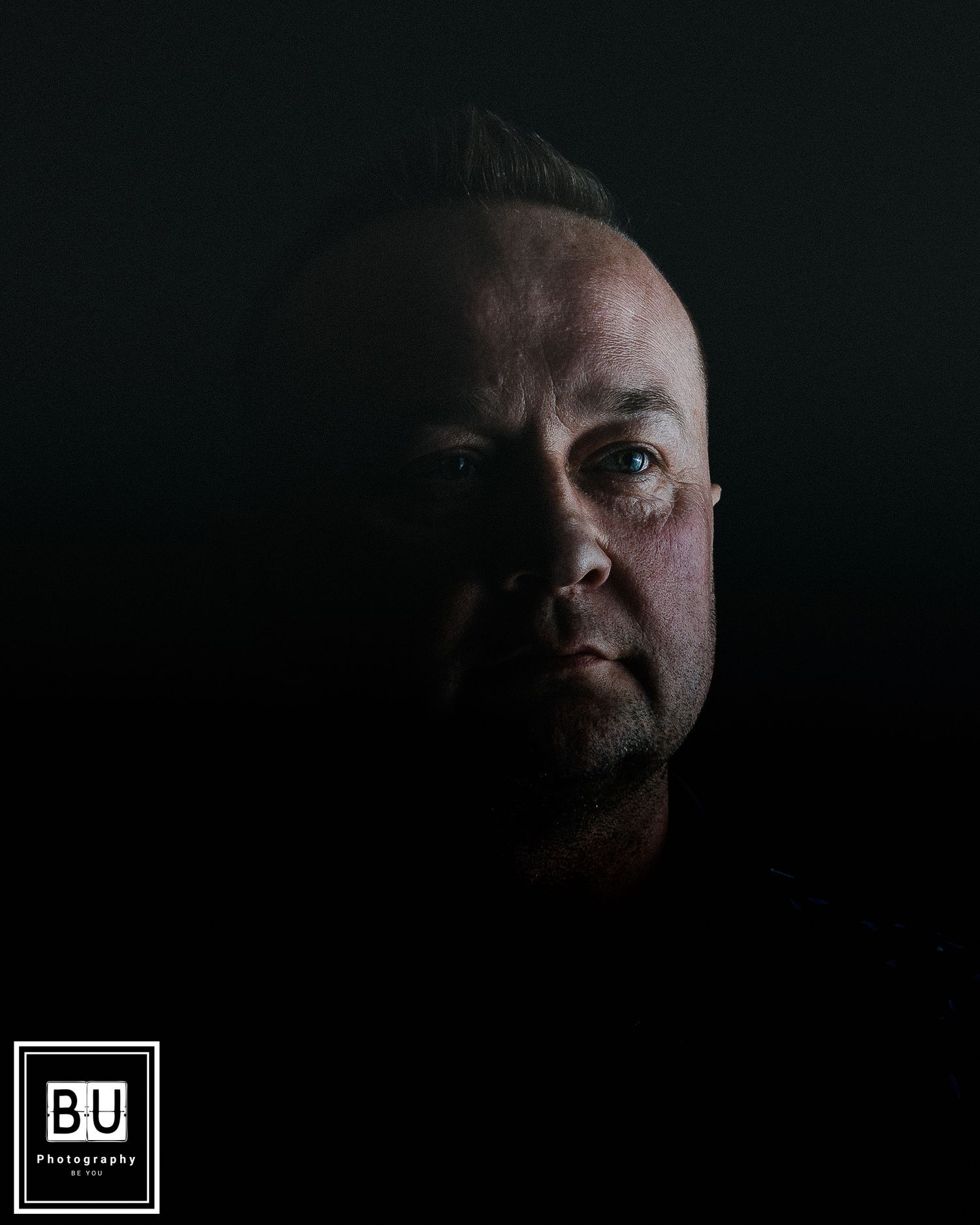 Low key dramatic portrait showing half of a face emerging from darkness with moody lighting.