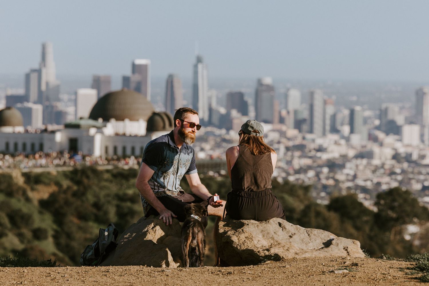 Man proposes to woman on a rocky hilltop overlooking the Griffith Observatory and Los Angeles skyline.