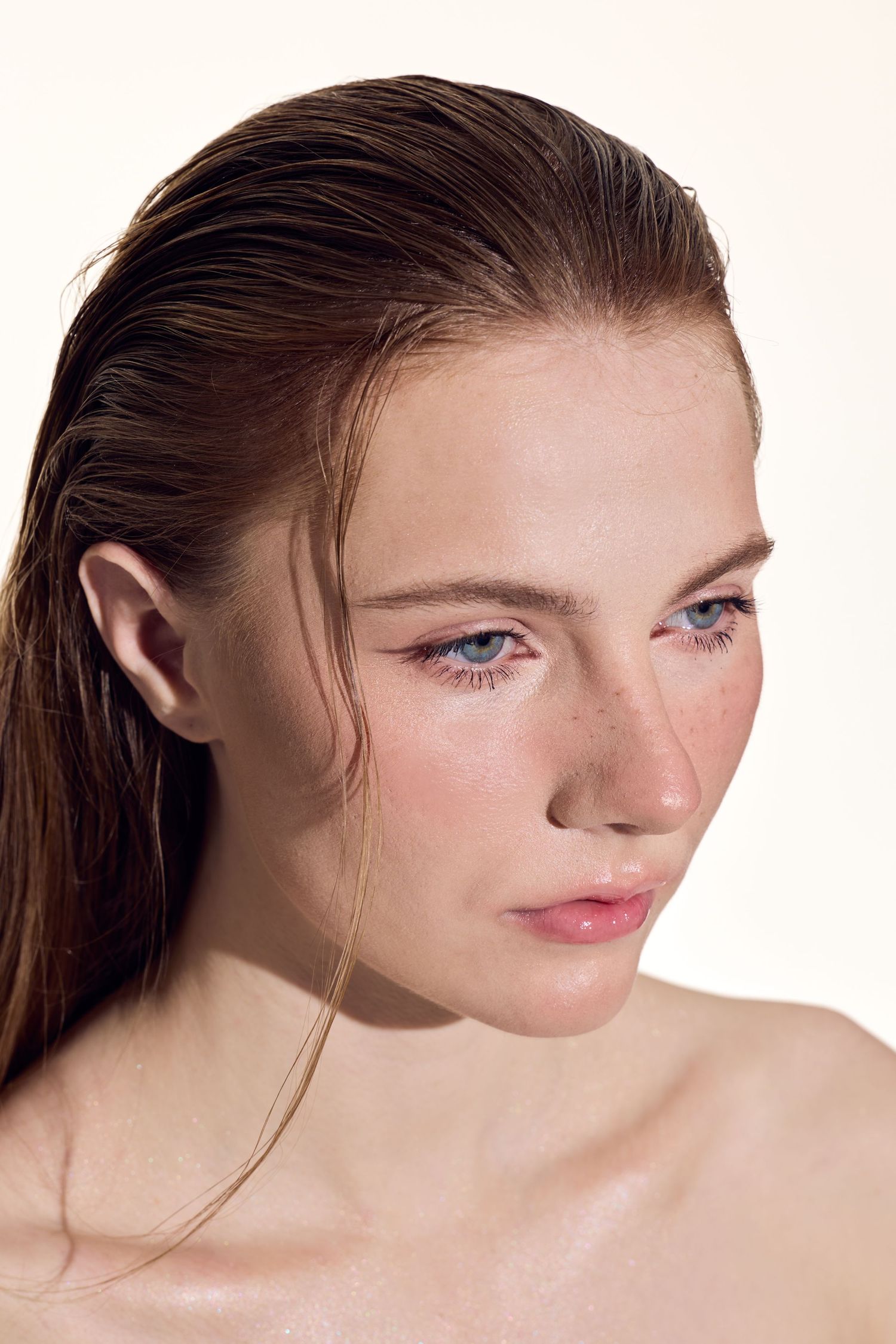 Beauty portrait of model with fresh dewy skin, blue eyes and natural makeup posing against light background.