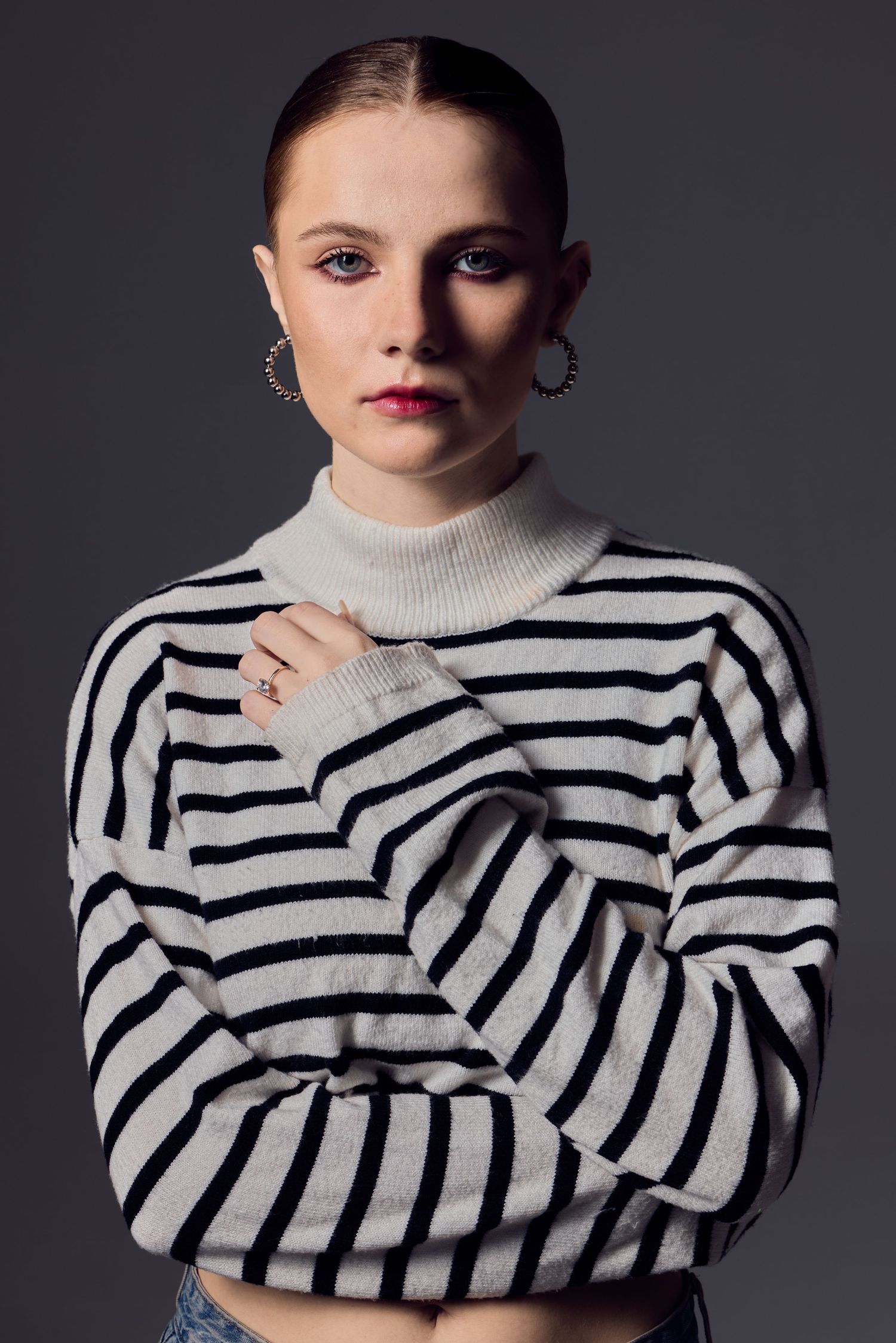 Portrait against dark background wearing black and white striped turtleneck sweater and silver hoop earrings.