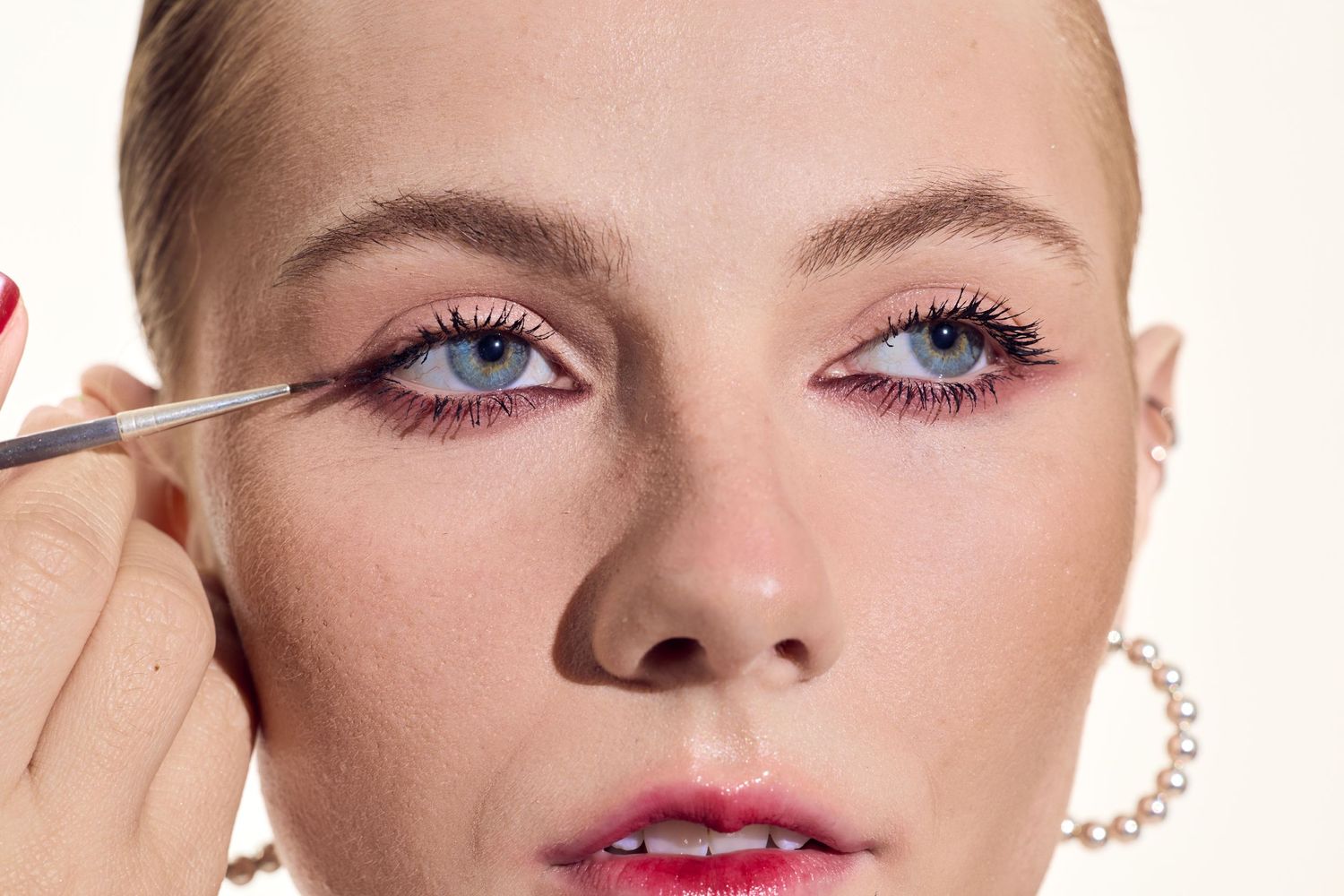 A close-up shot showing the application of pink eyeshadow with a small brush during a beauty makeup tutorial.