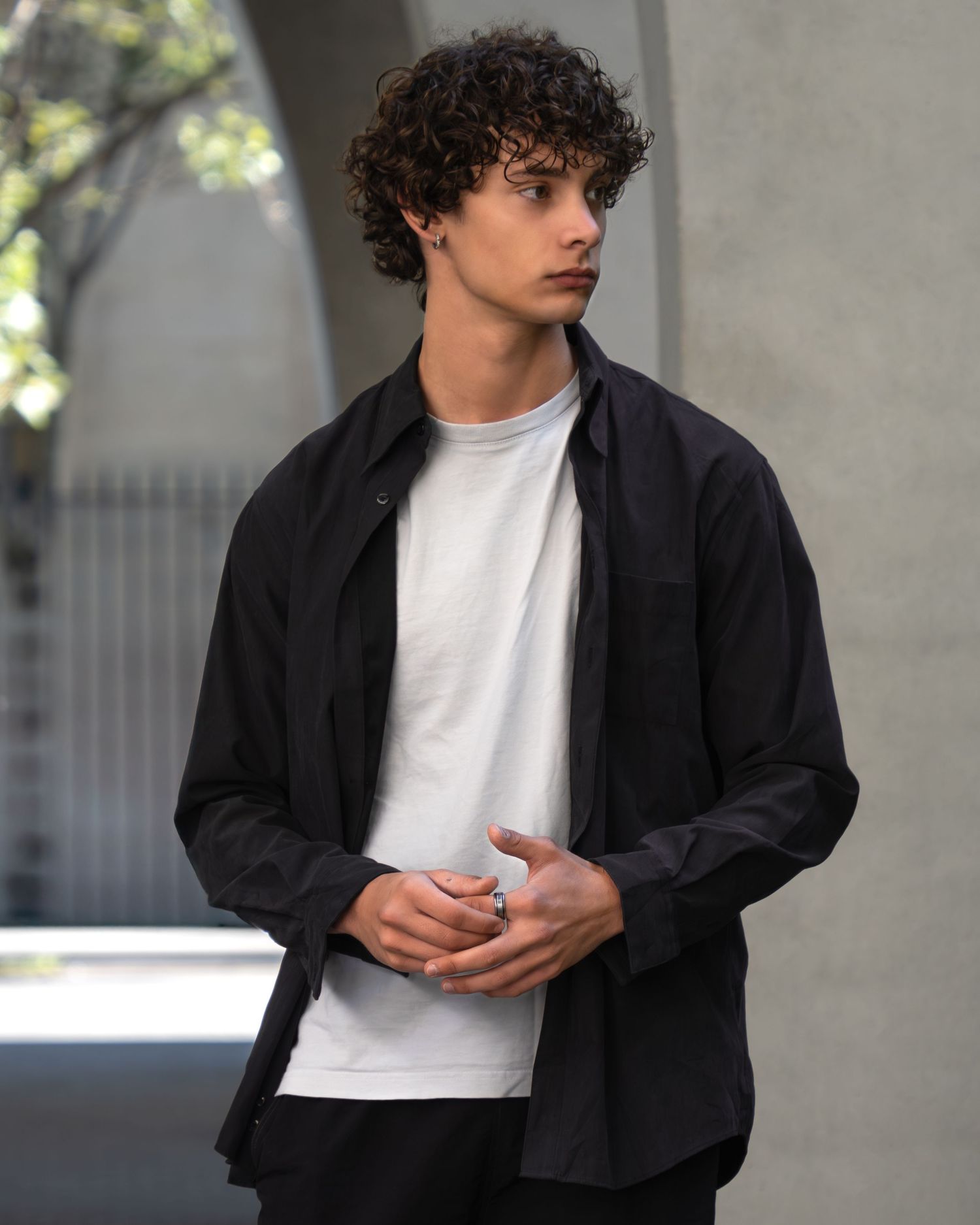 Person in a black jacket and white t-shirt seen from different angles standing against a light background.