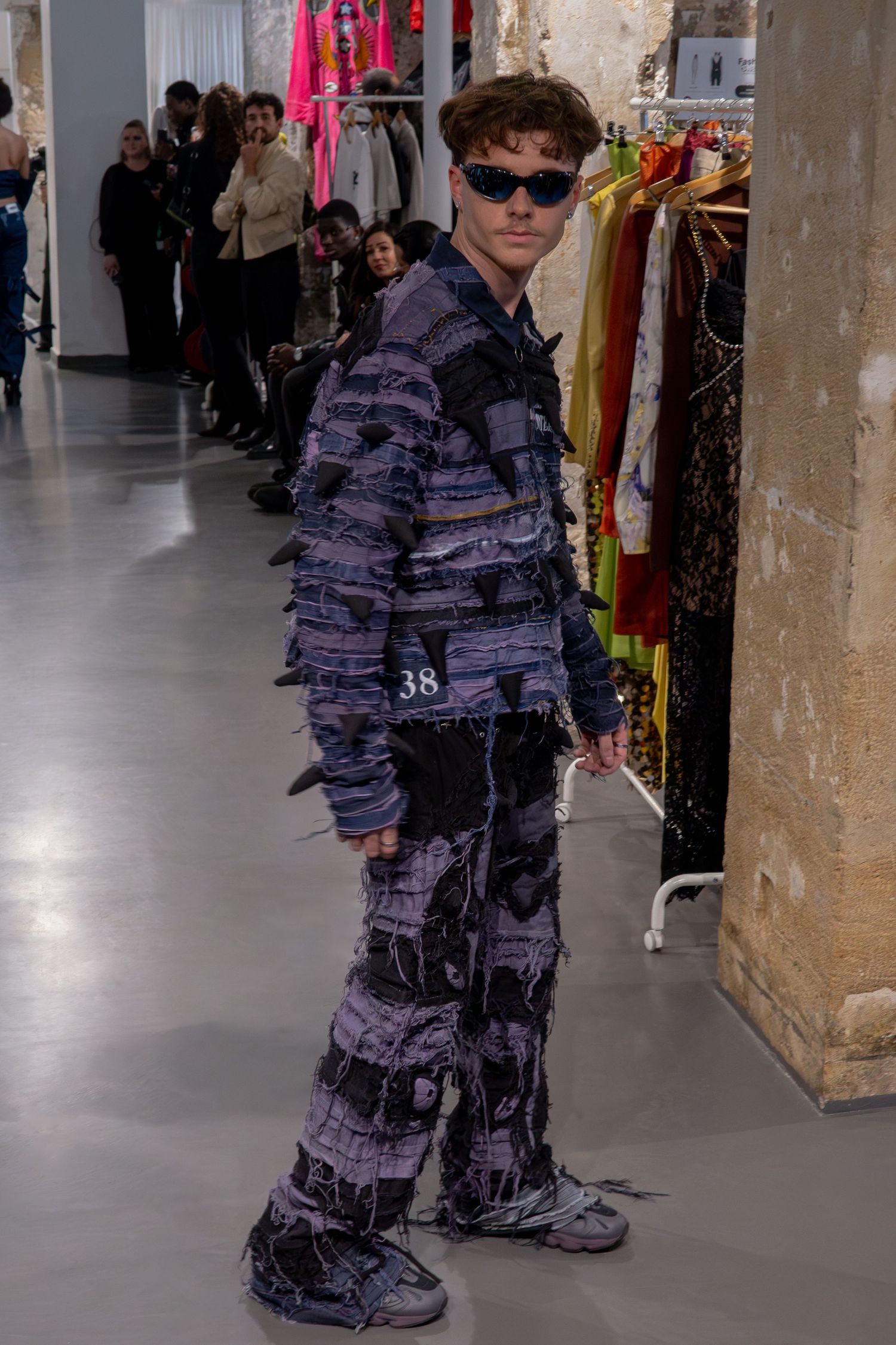 Ensemble streetwear patchwork violet avec lunettes de soleil présenté sur un défilé de mode pour la Paris Fashion Week.