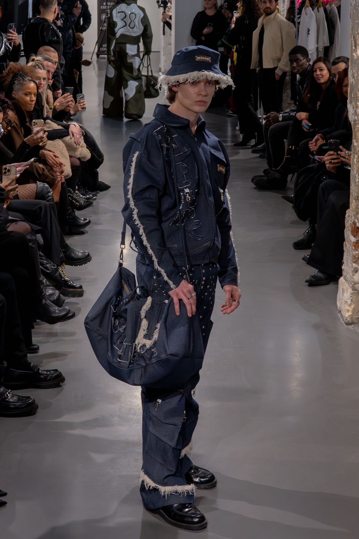 Tenue d'inspiration workwear bleu marine avec chapeau bob et sac messager sur un défilé de mode lors de la Paris Fashion Week.