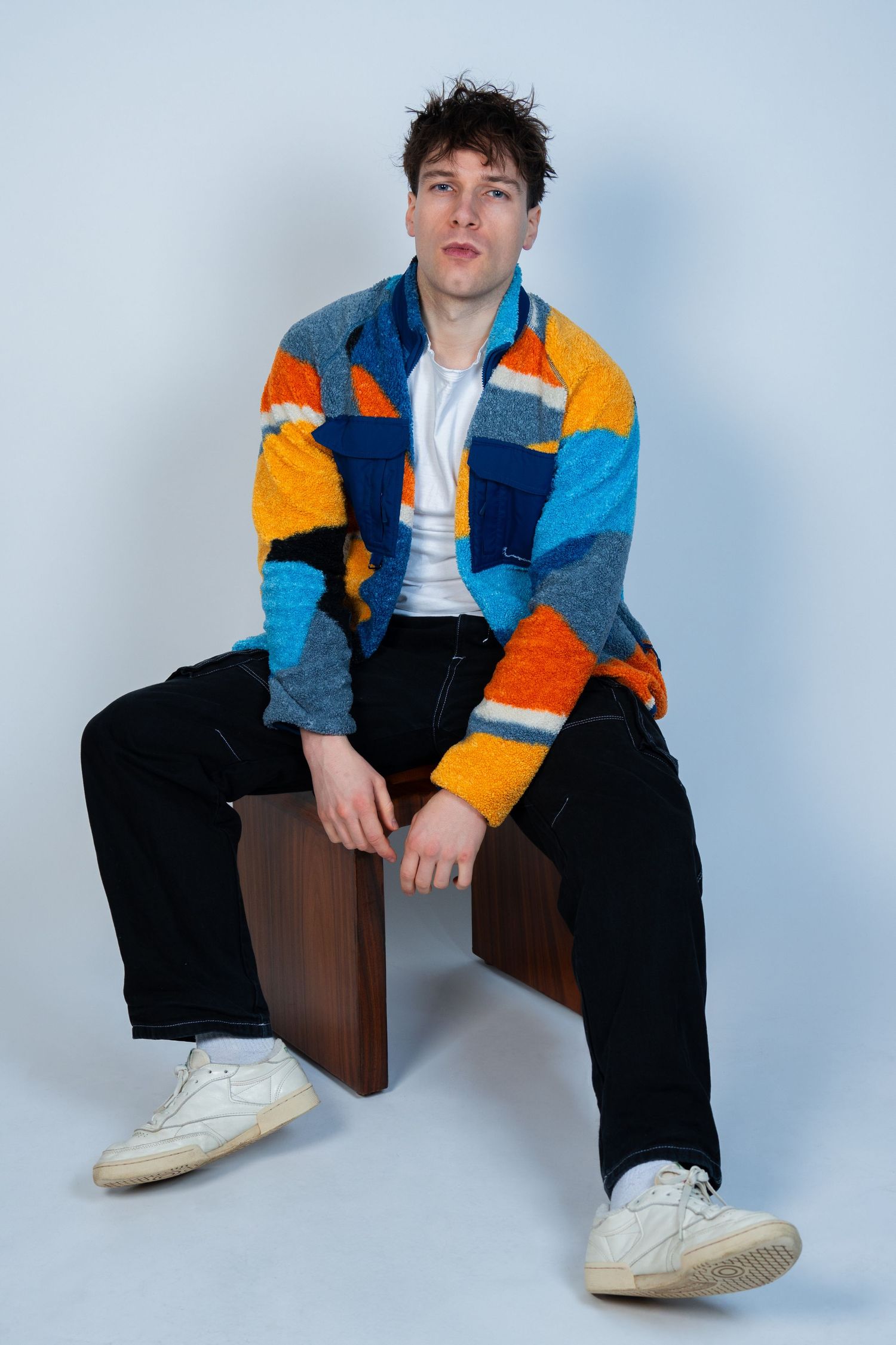 Modèle portant une veste polaire à rayures colorées et un débardeur blanc en studio.