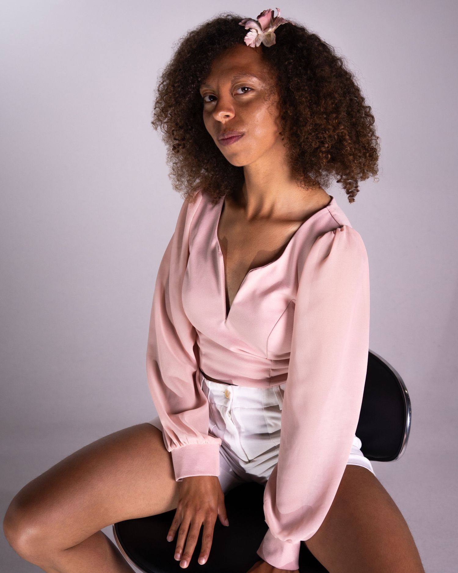 Model in pink wrap blouse poses against purple backdrop in artistic fashion photoshoot series.