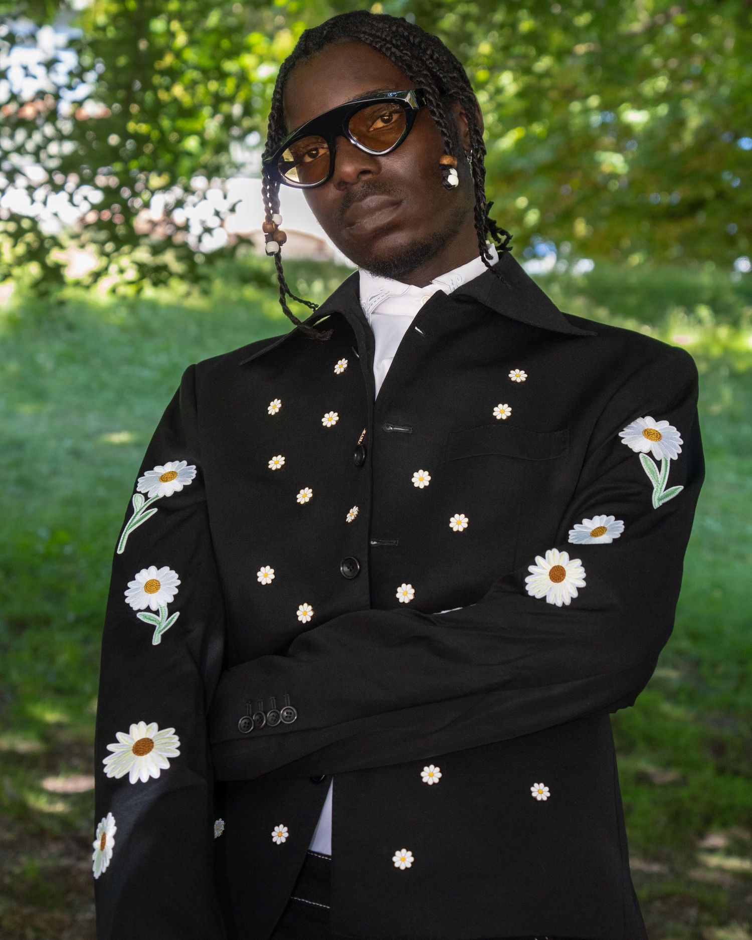 Elegant black blazer decorated with embroidered daisies worn with glasses and a white dress shirt in an outdoor setting.