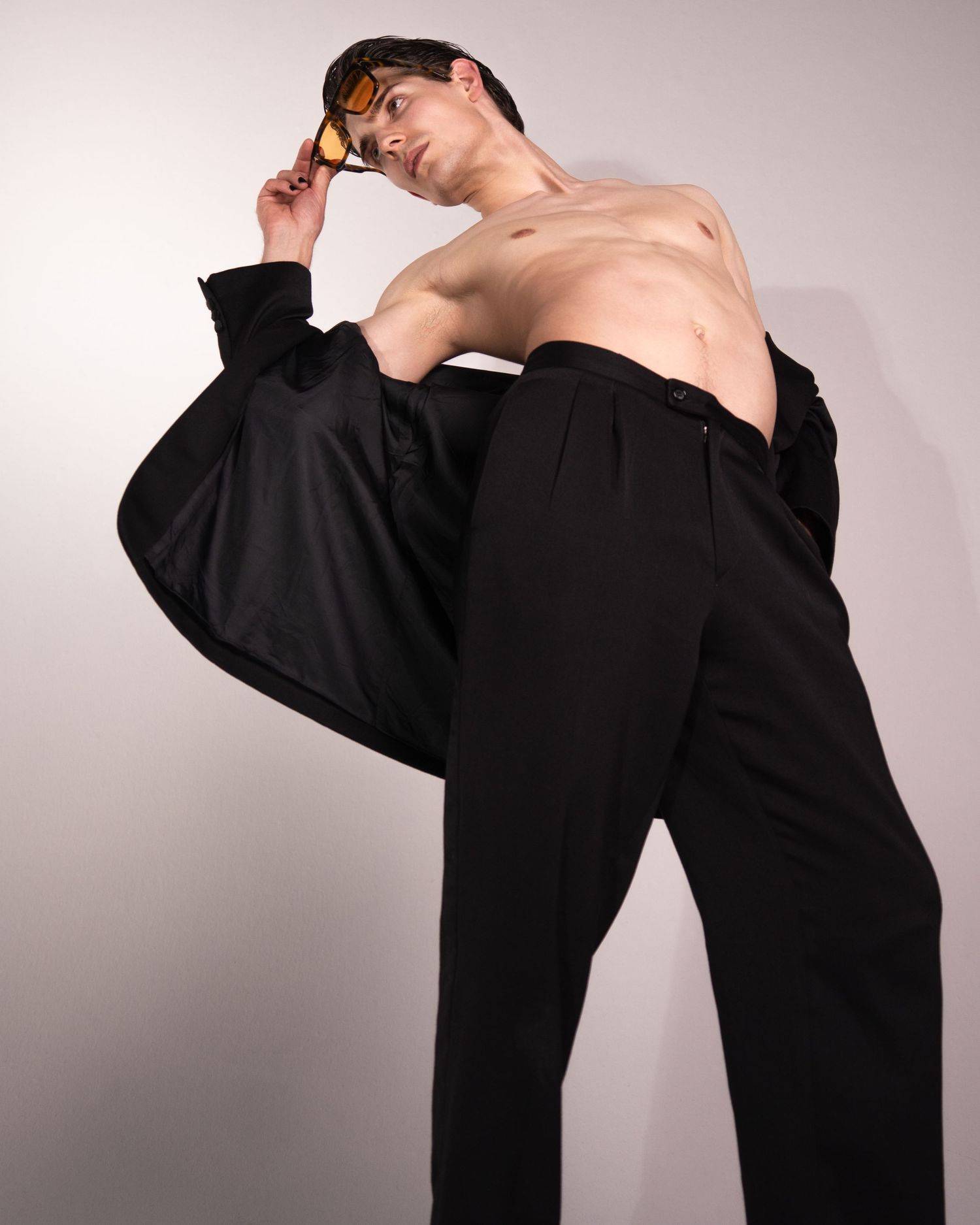 Person in a flowing black blouse strikes a graceful dance-like pose in front of a light gray studio backdrop.