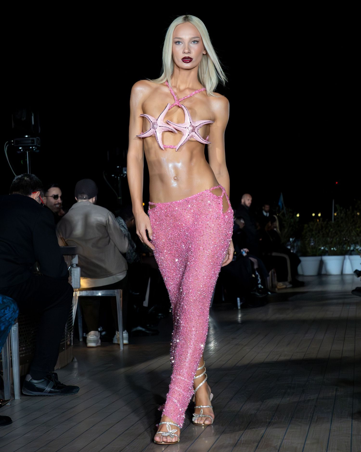 Un mannequin défile sur un podium vêtu d'un pantalon à paillettes roses et de sandales à lanières lors de la Paris Fashion Week.