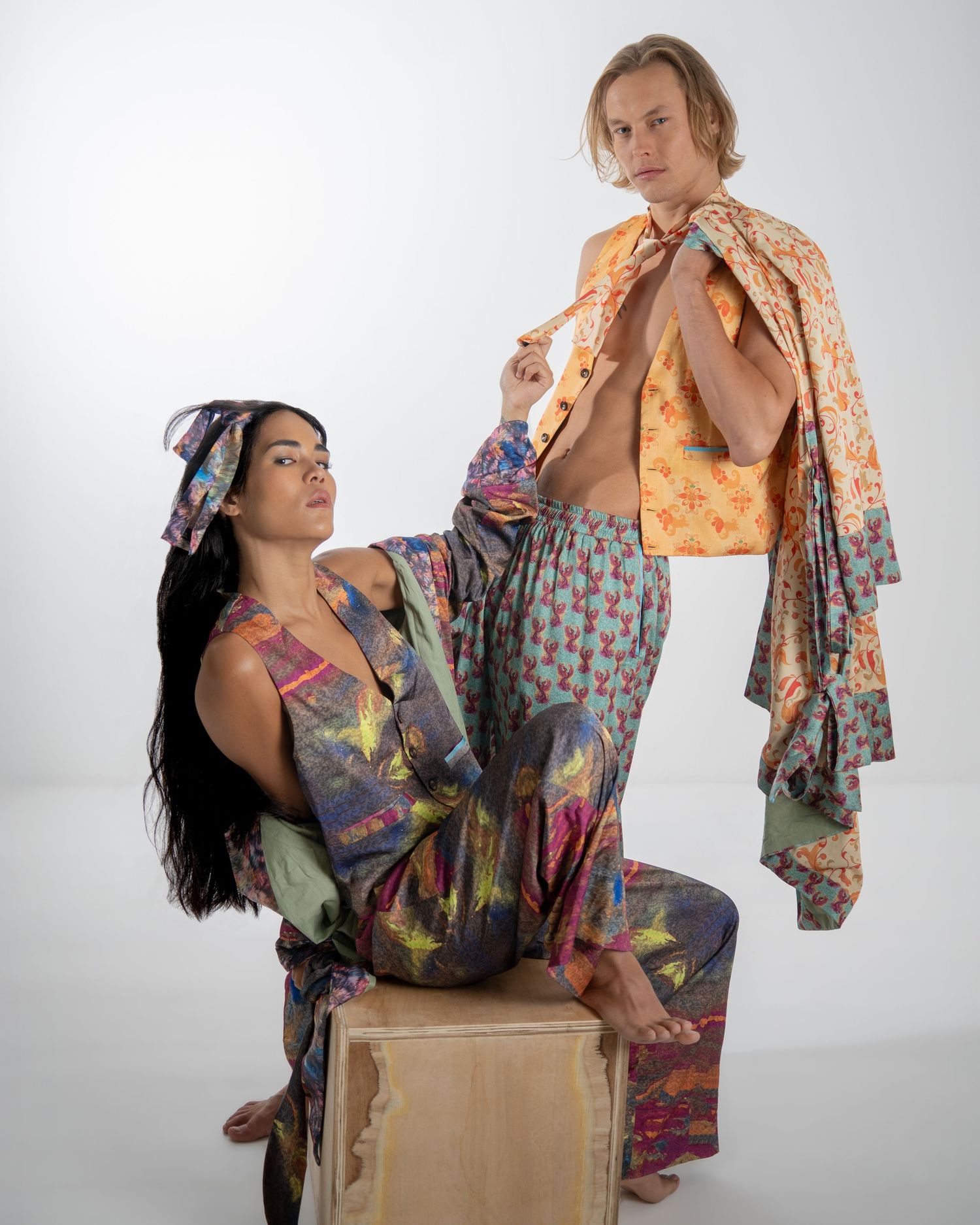 Two models pose artistically in vibrant floral prints against a white backdrop for a fashion photoshoot.