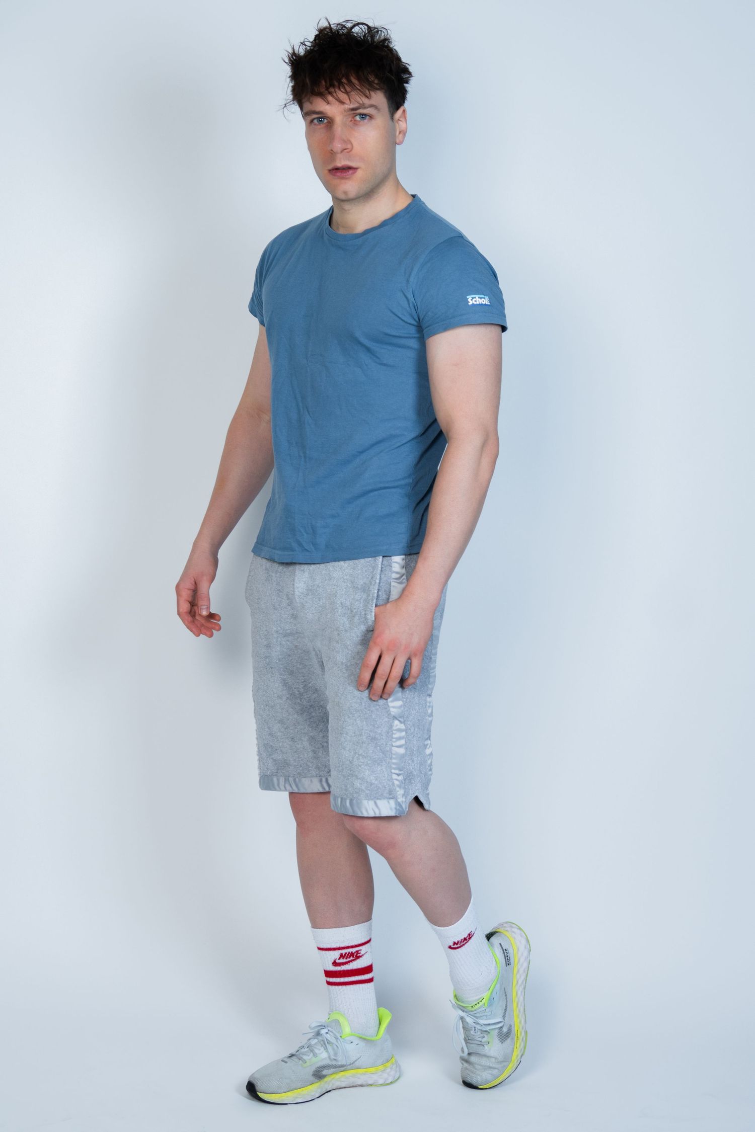 Le mannequin décontracté pose en t-shirt bleu ajusté et short délavé jusqu'aux genoux avec des baskets de sport.