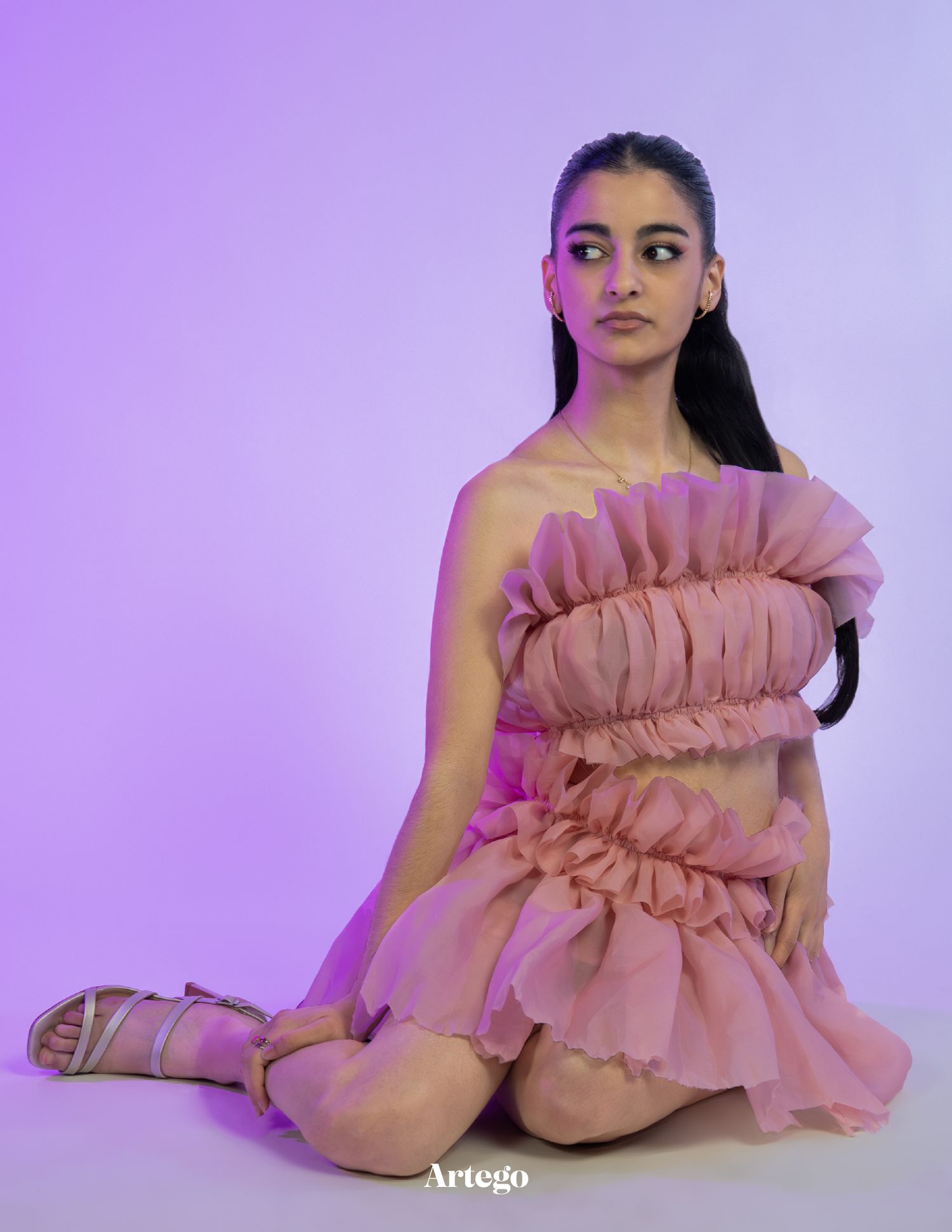 Figure in pink ruffled dress poses artistically against purple backdrop in fashion editorial series.