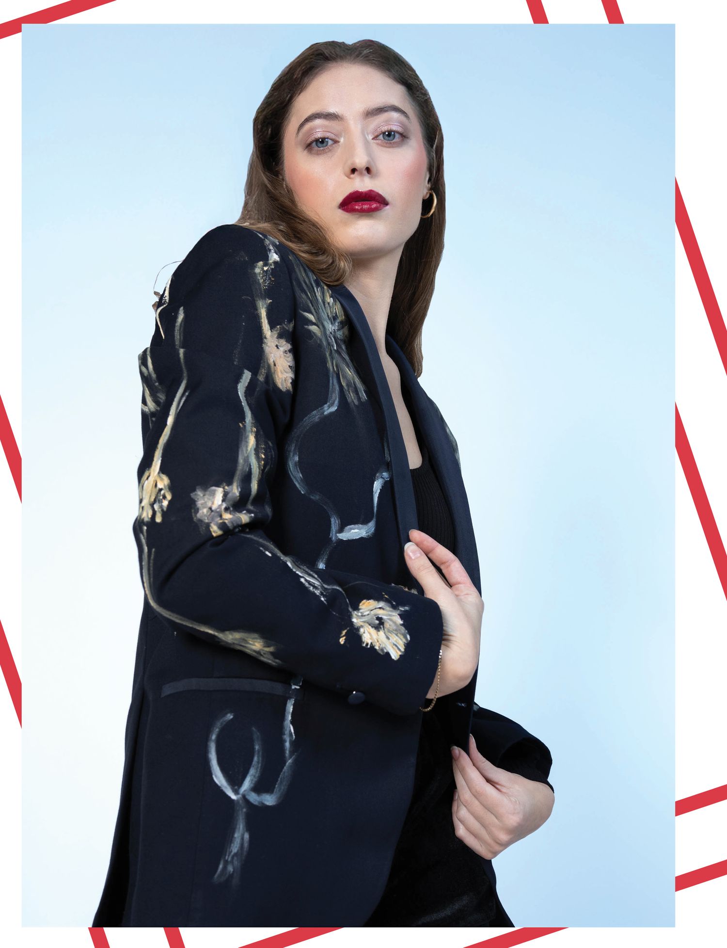 Fashion model wearing black floral printed jacket poses against light blue background with red frame.