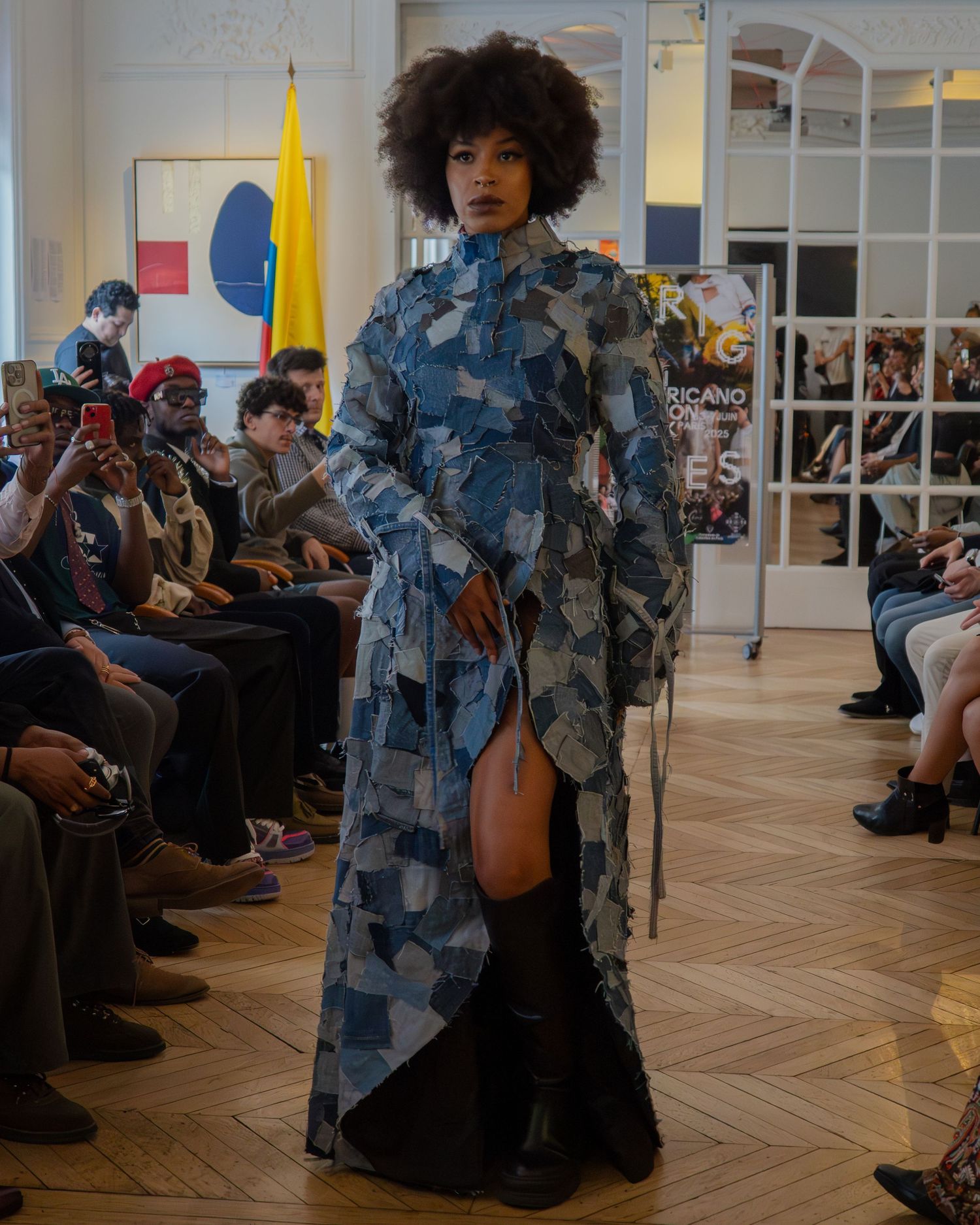 A model walks the runway in a dramatic blue patterned dress with a high slit at a fashion show event.